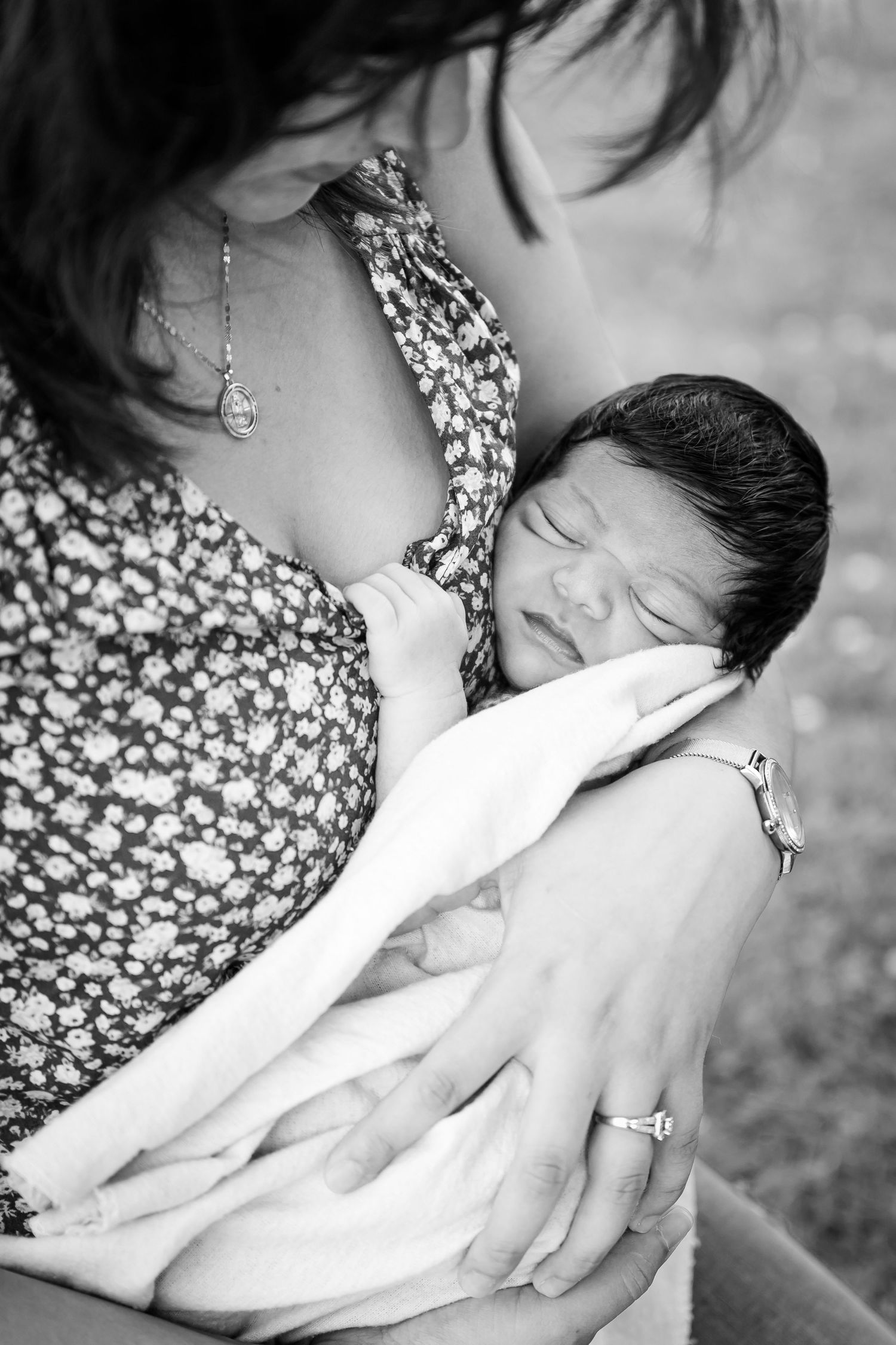 A tender moment captured in black and white showing a parent cradling a newborn in a floral print dress.