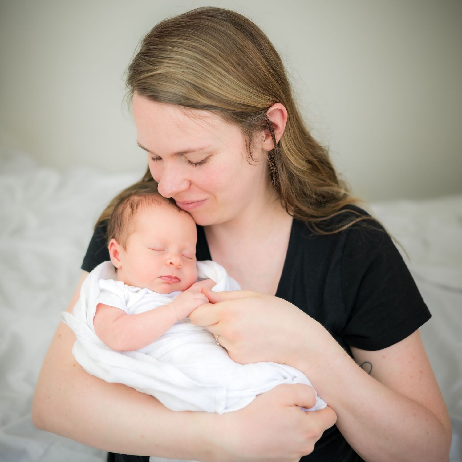 A tender moment between parent and newborn baby as they cuddle together on a bed.
