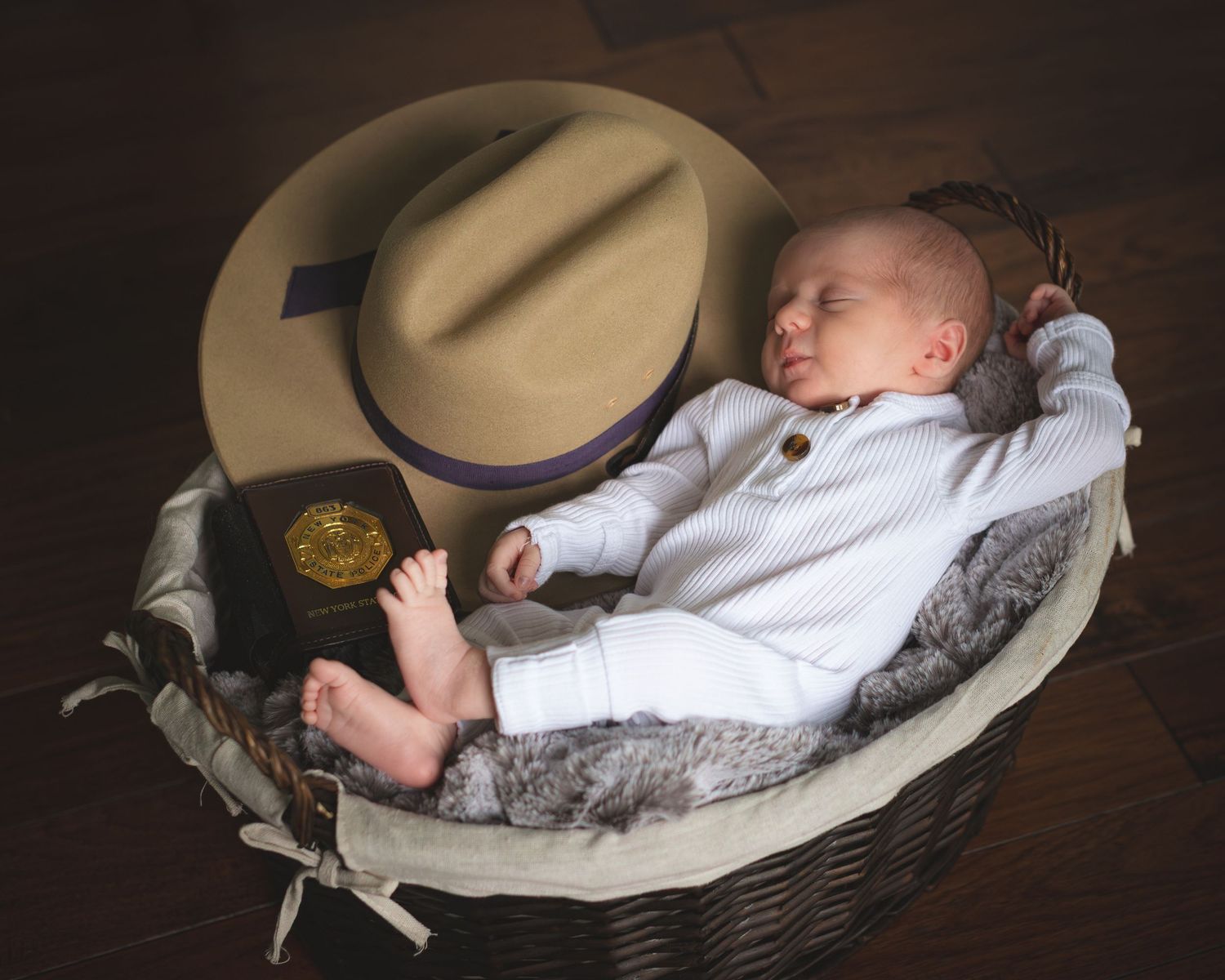 A sleeping baby rests in a woven basket with a tan cowboy hat and white clothing against a dark background.