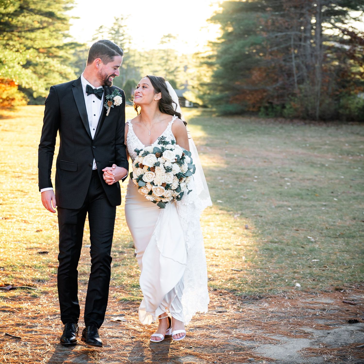 A romantic golden hour wedding photo shows a couple walking together on a forest path while sharing a joyful moment.