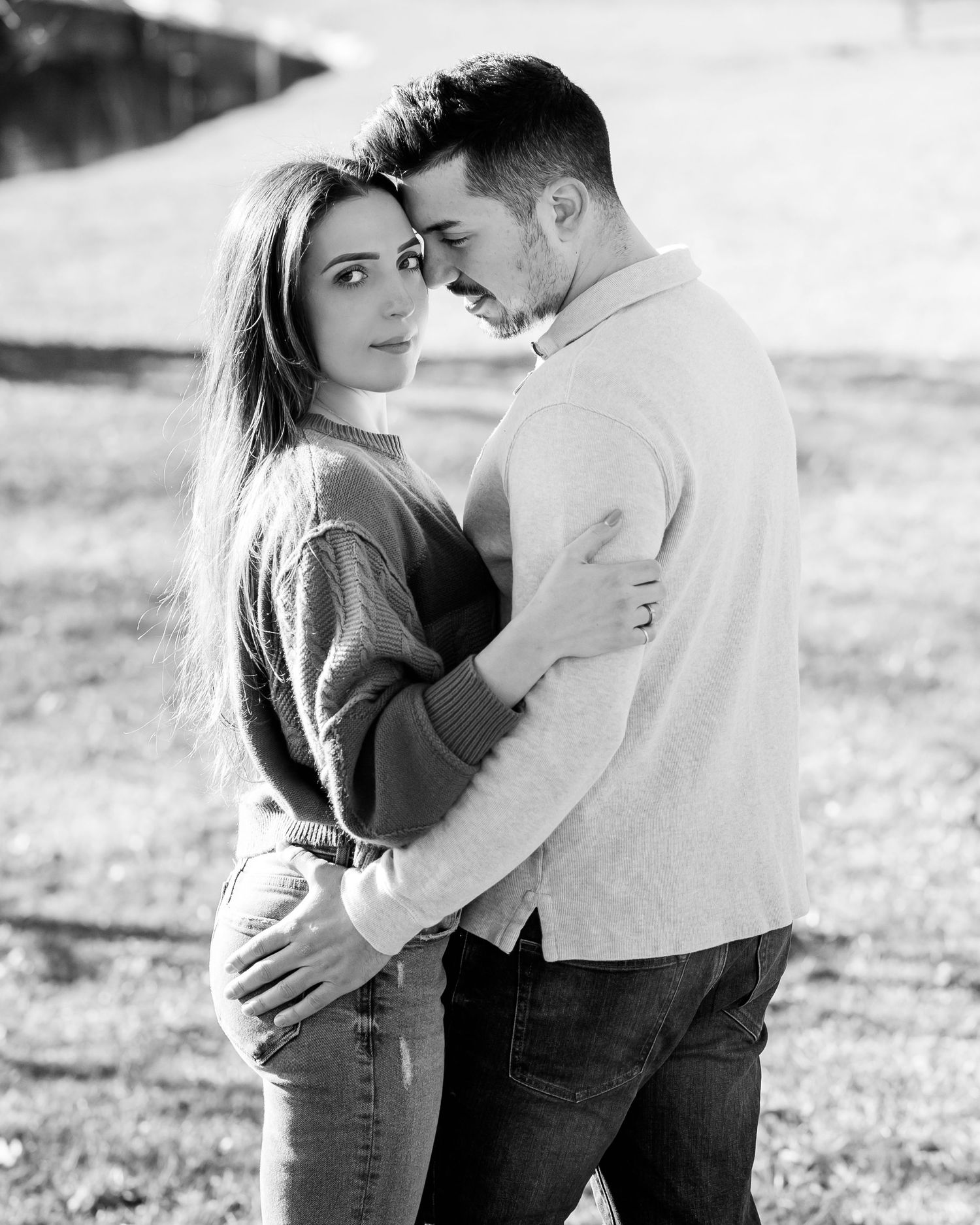 Black and white portrait photograph of an intimate romantic couple embracing outdoors in casual clothing.