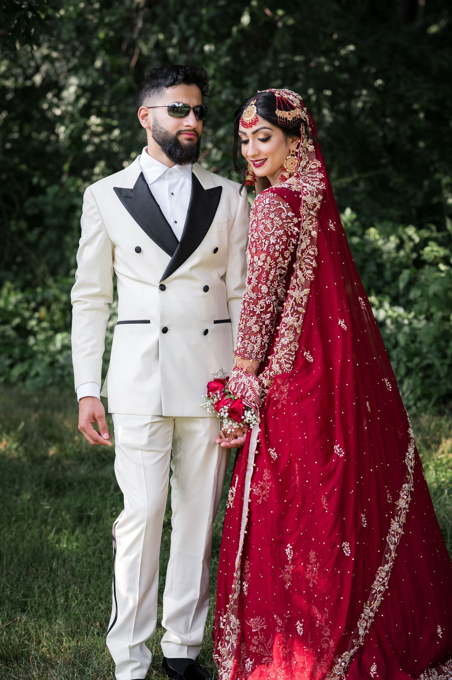 Elegant couple in South Asian wedding attire featuring white suit and red embellished lehenga.