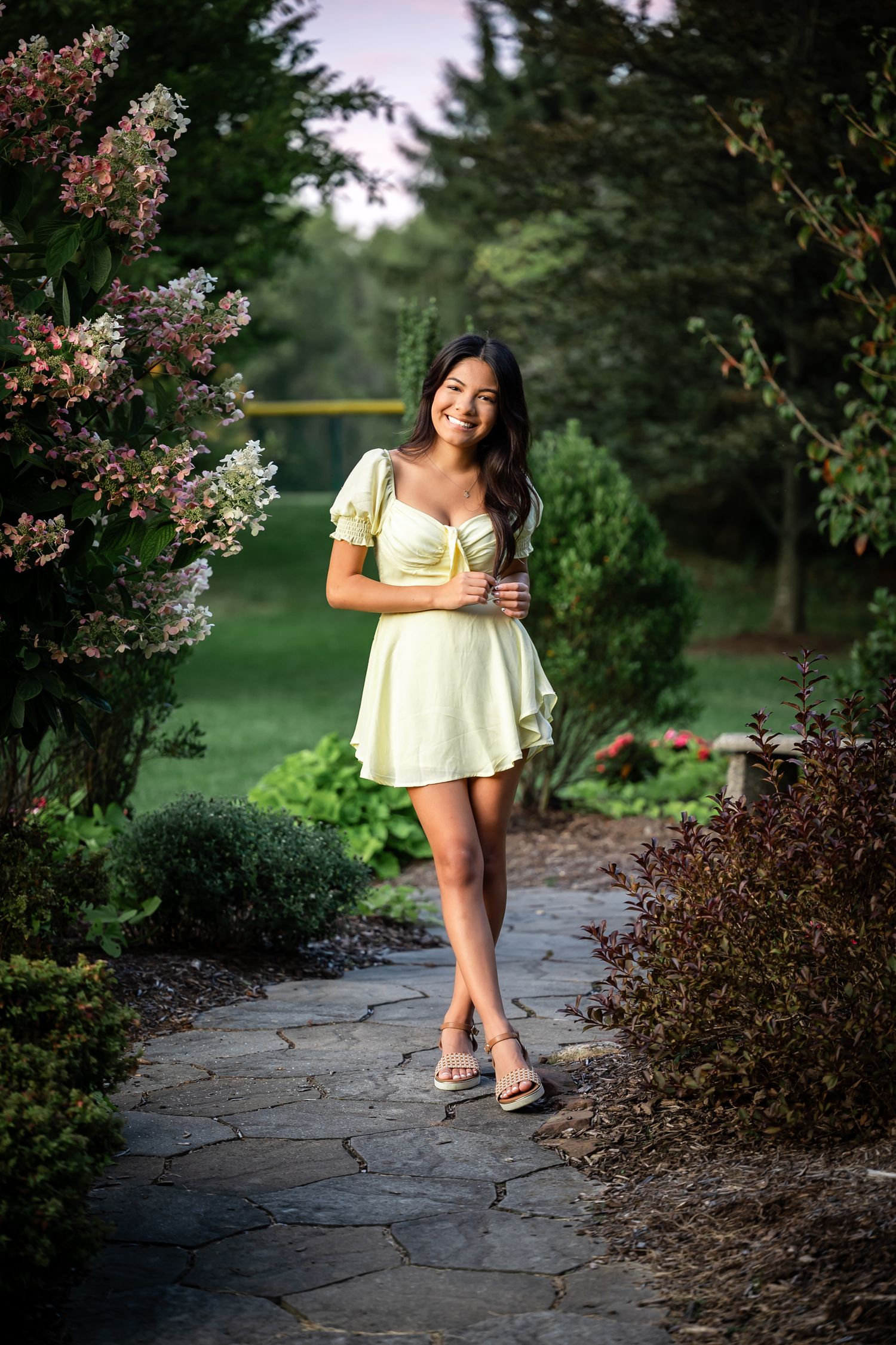 Light yellow summer dress against lush garden background with blooming flowers.