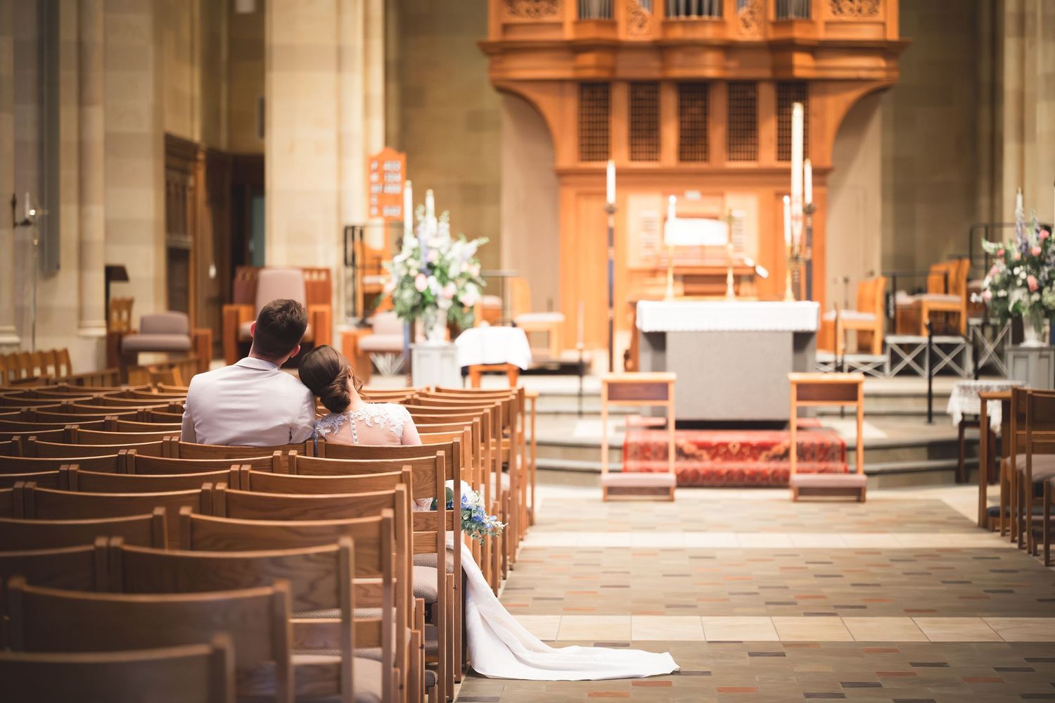 Bride and groom sitting together in church pews before a beautifully decorated altar during a wedding ceremony.