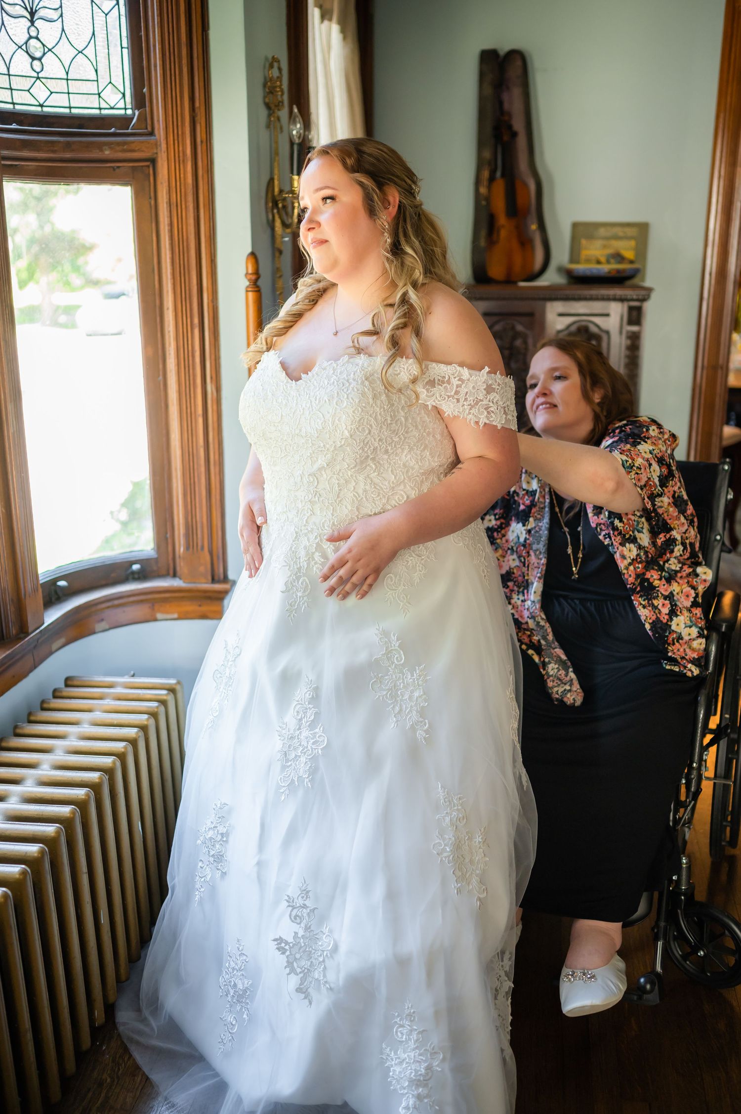 Wedding dress fitting session near window with vintage radiator and violin decoration.