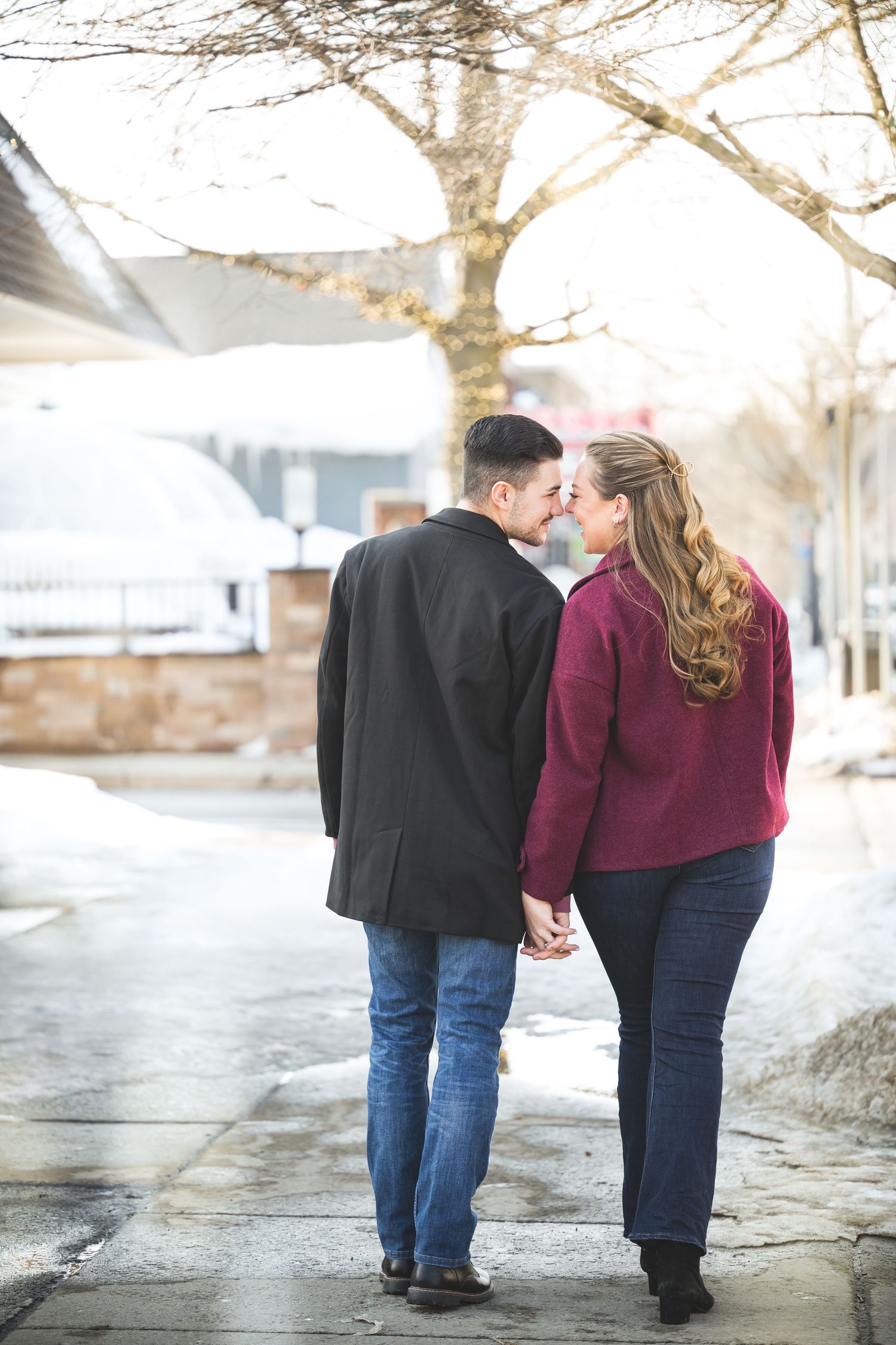 Engaged couple holding hands walking down snowy sidewalk in winter.
