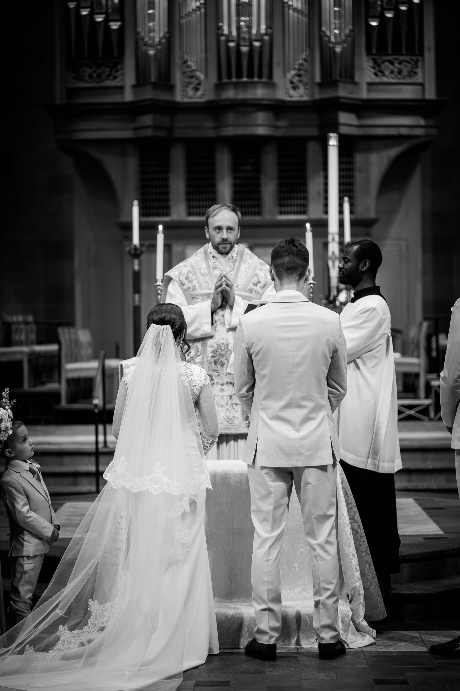 Bride and groom exchange vows before a priest at a church altar in a classic black and white photo.
