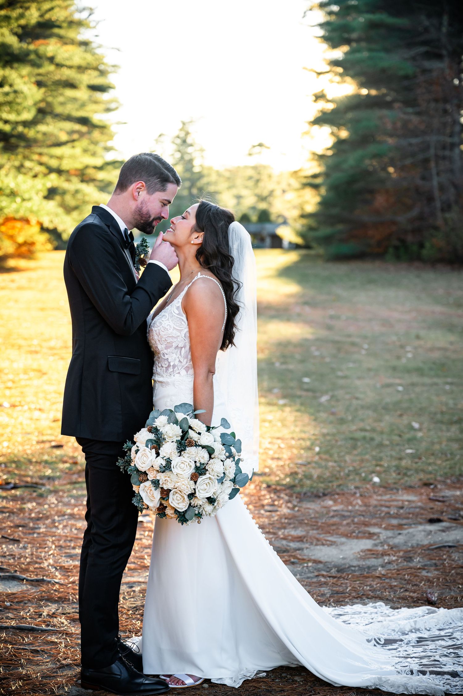 A couple shares an intimate moment at their wedding with evergreen trees and golden sunlight in the background.