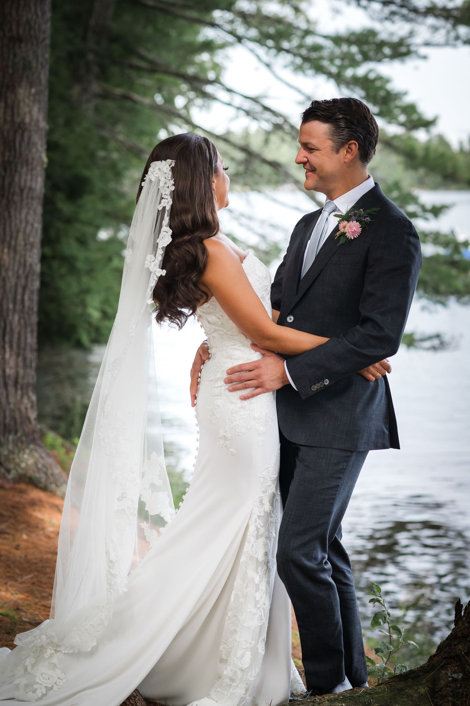 A waterfront wedding portrait among pine trees with a flowing white veil.