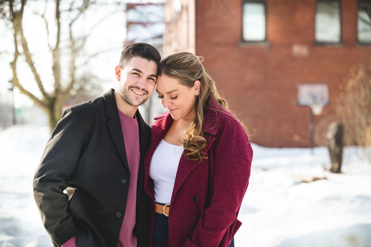 Smiling couple posing together outdoors in winter, wearing stylish coats with snow in the background.