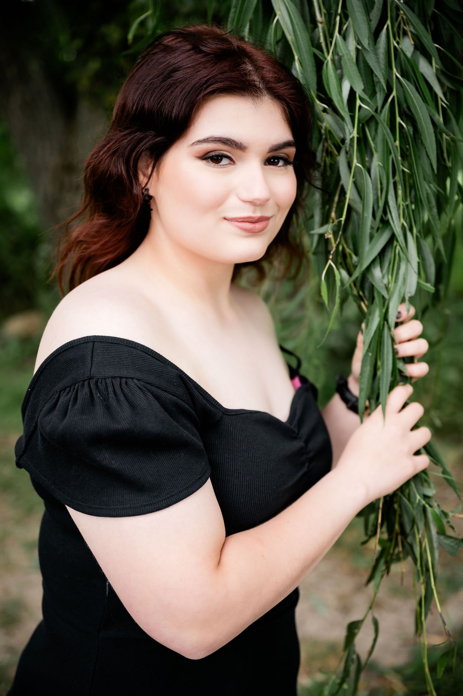 Artistic portrait captured among drooping willow branches with soft natural lighting.