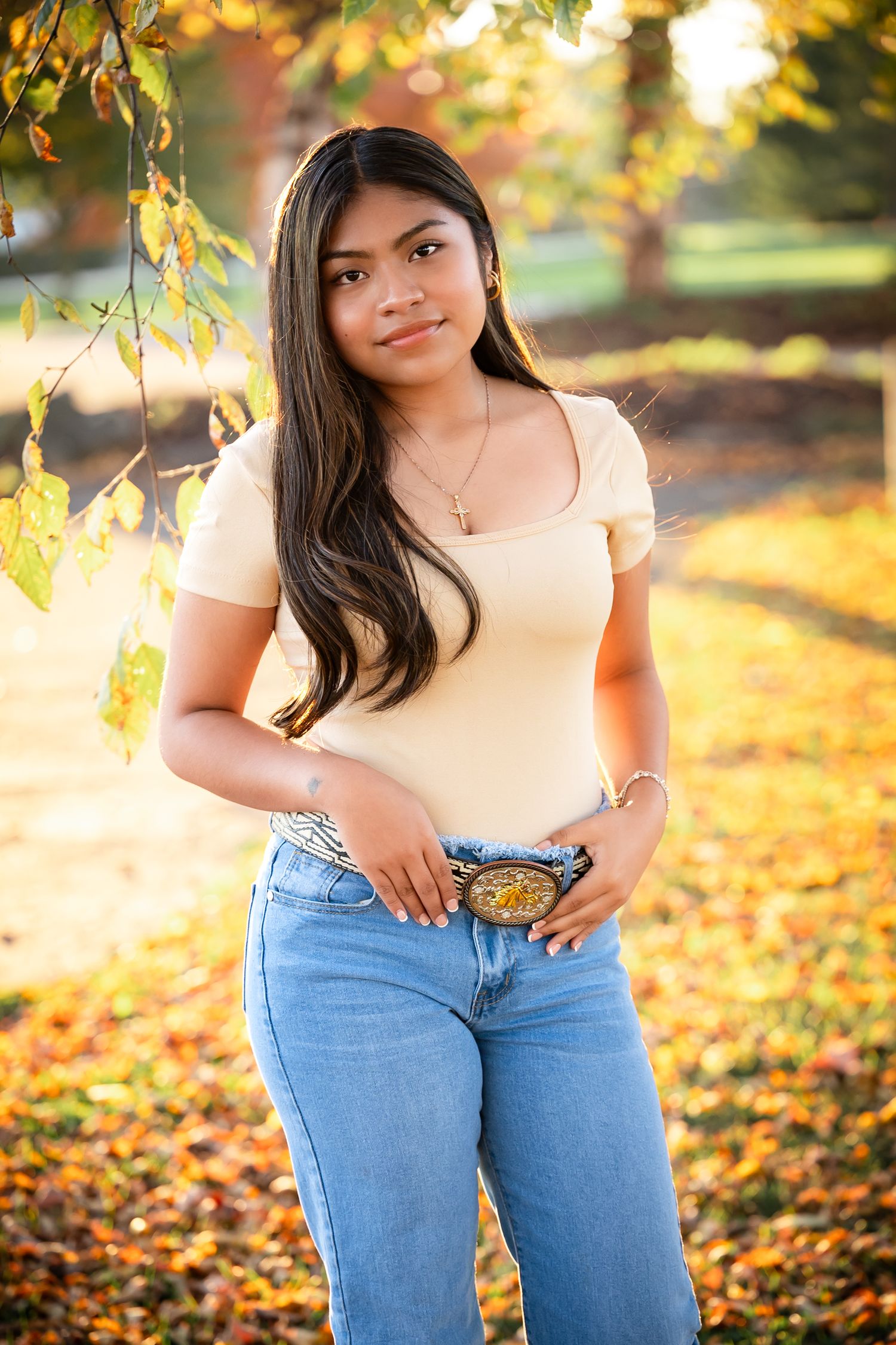 Autumn portrait session in a park with golden leaves and sunlight filtering through trees in the background.