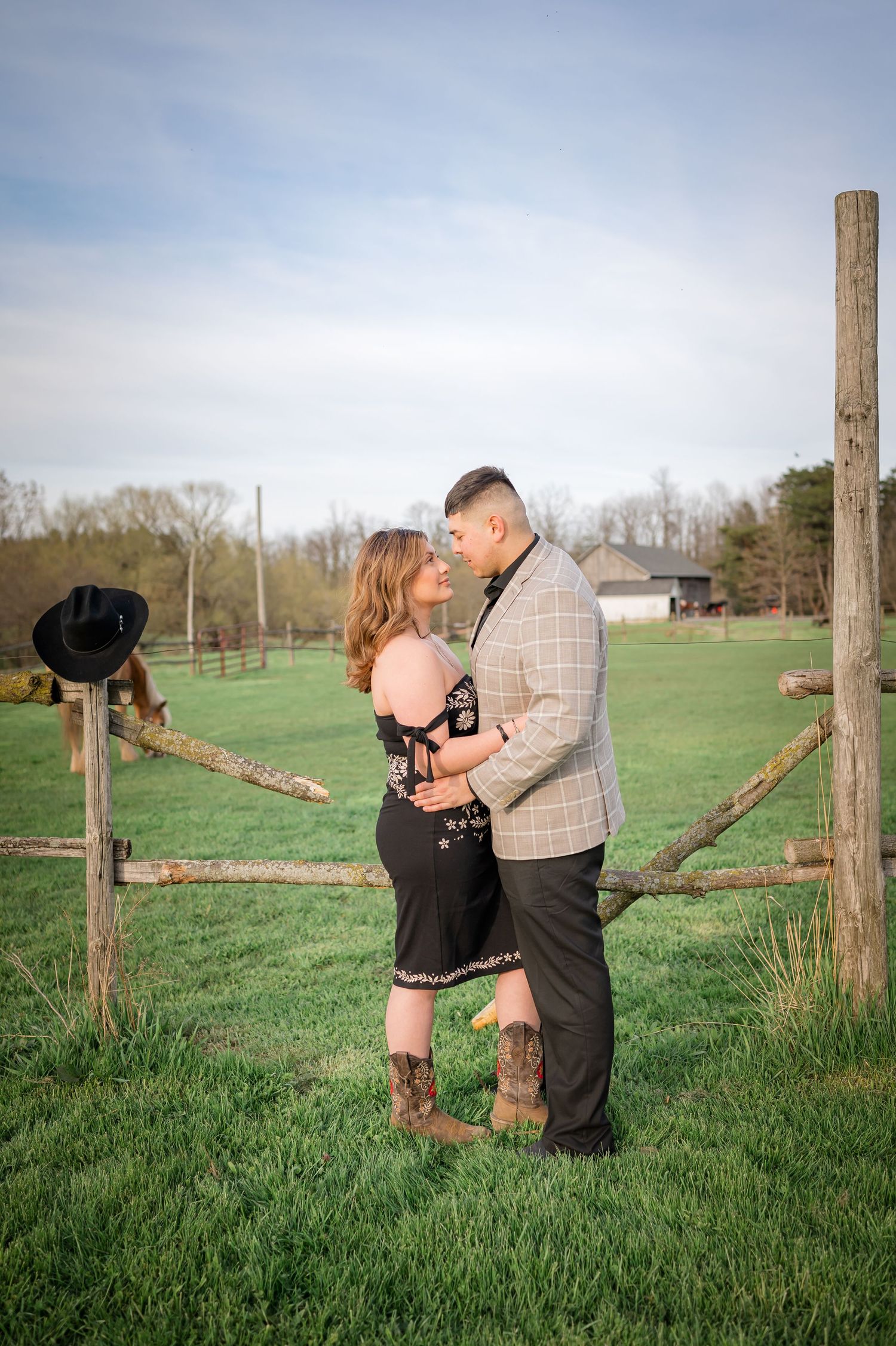 A romantic embrace between a couple by a wooden fence post in a green field.