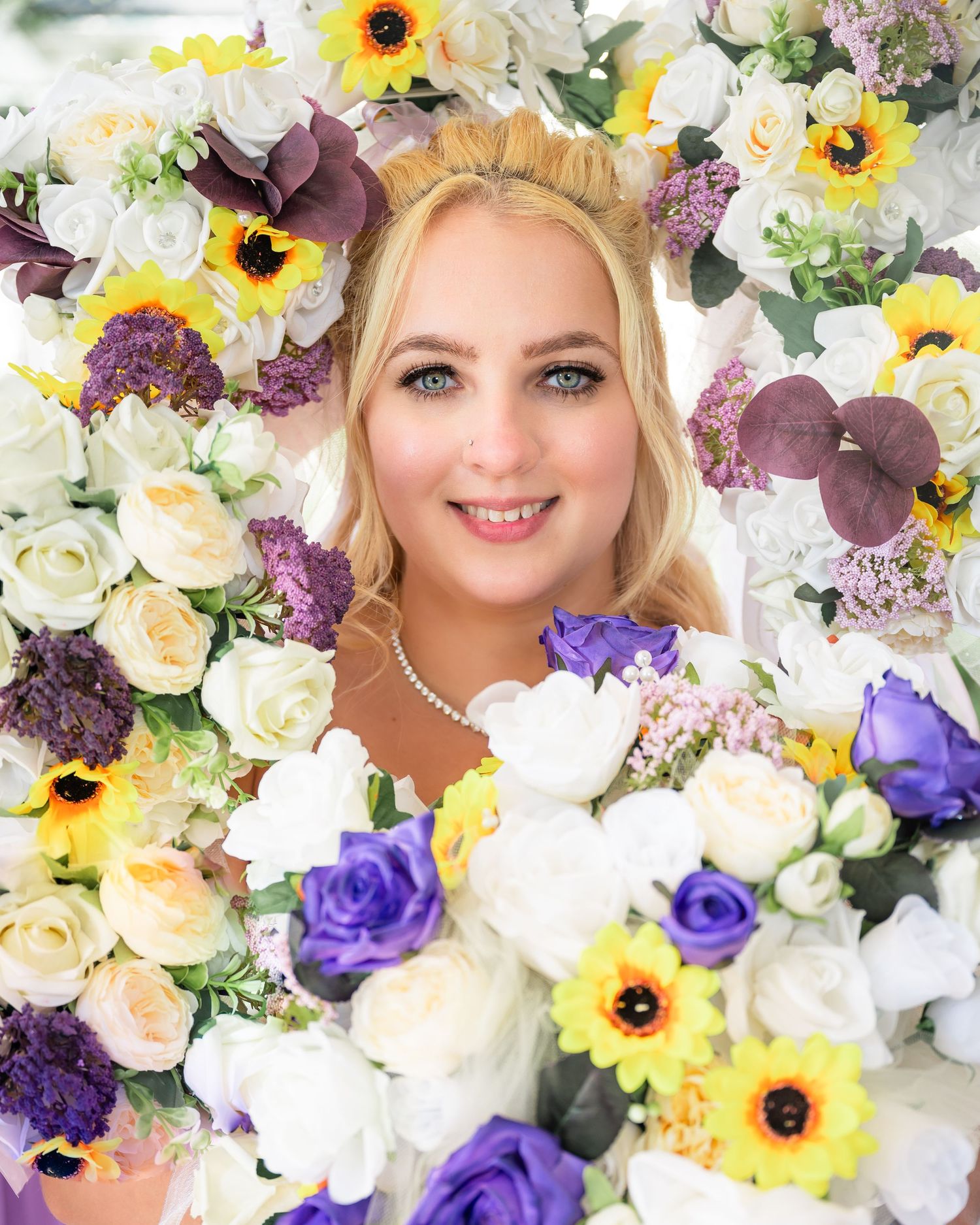 Colorful floral arrangement with sunflowers, roses and purple blooms frames a bridal portrait.