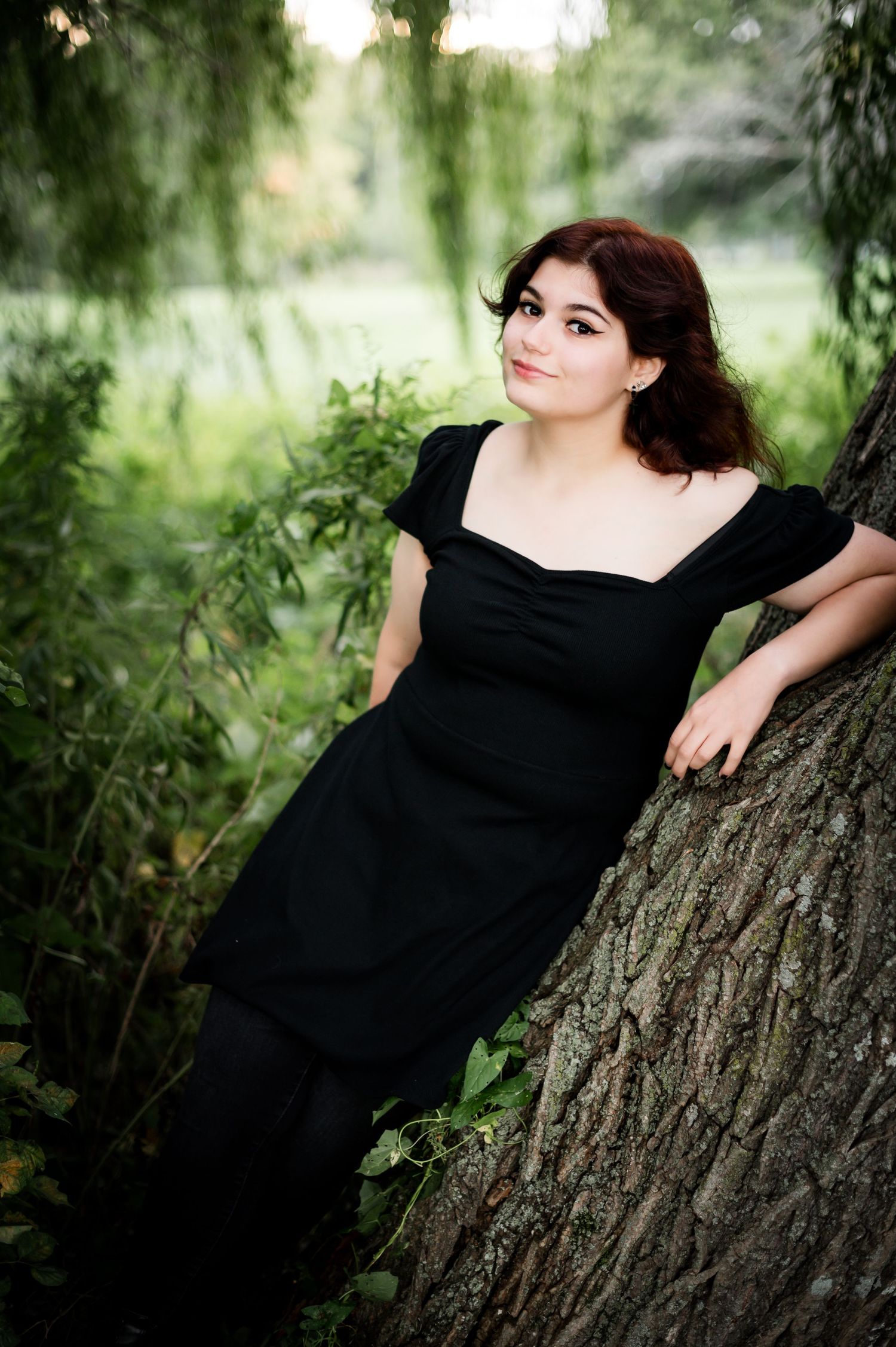 Dramatic portrait against a willow tree trunk with soft bokeh background in a garden setting.