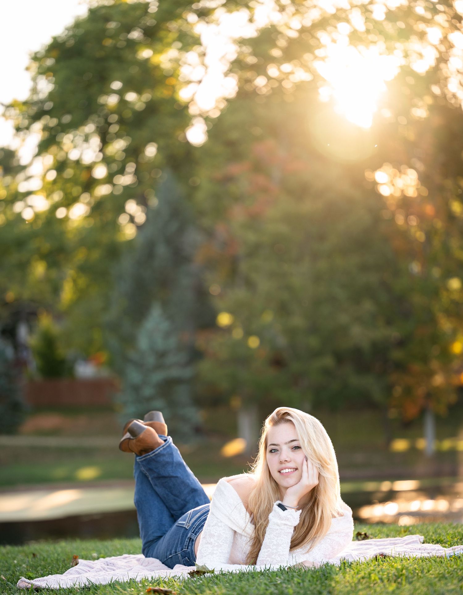 Young woman in white sweater lying on grass during golden hour sunset in autumn park.