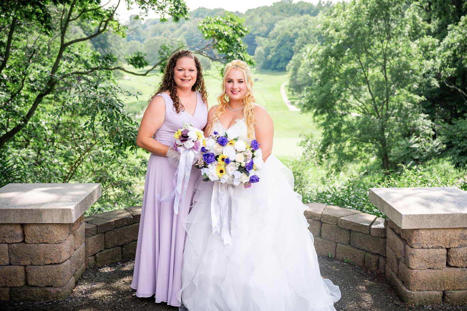 Wedding party members pose with bouquets on a scenic stone overlook.