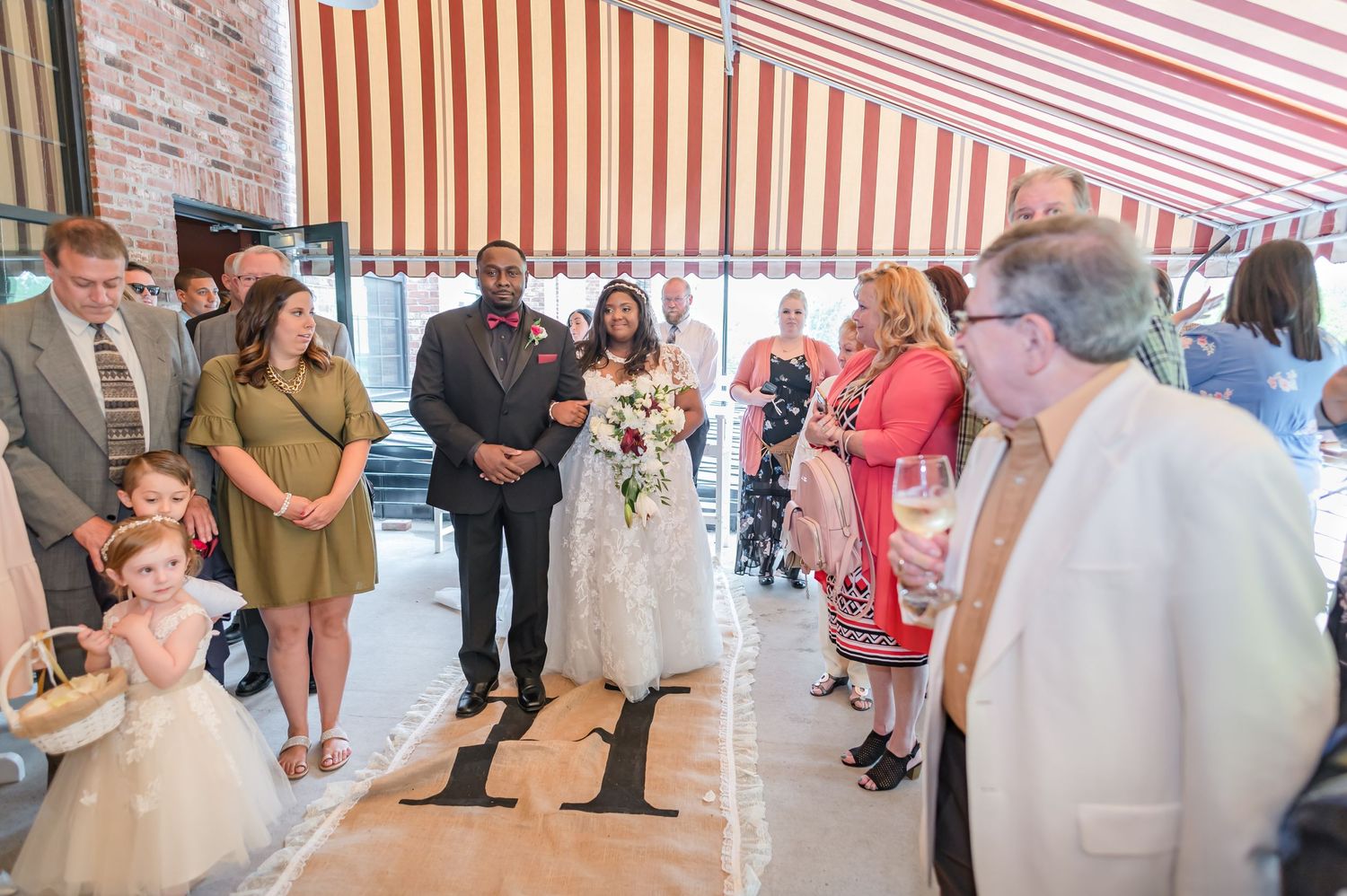 Wedding guests gather under a striped awning during the ceremony proceedings.