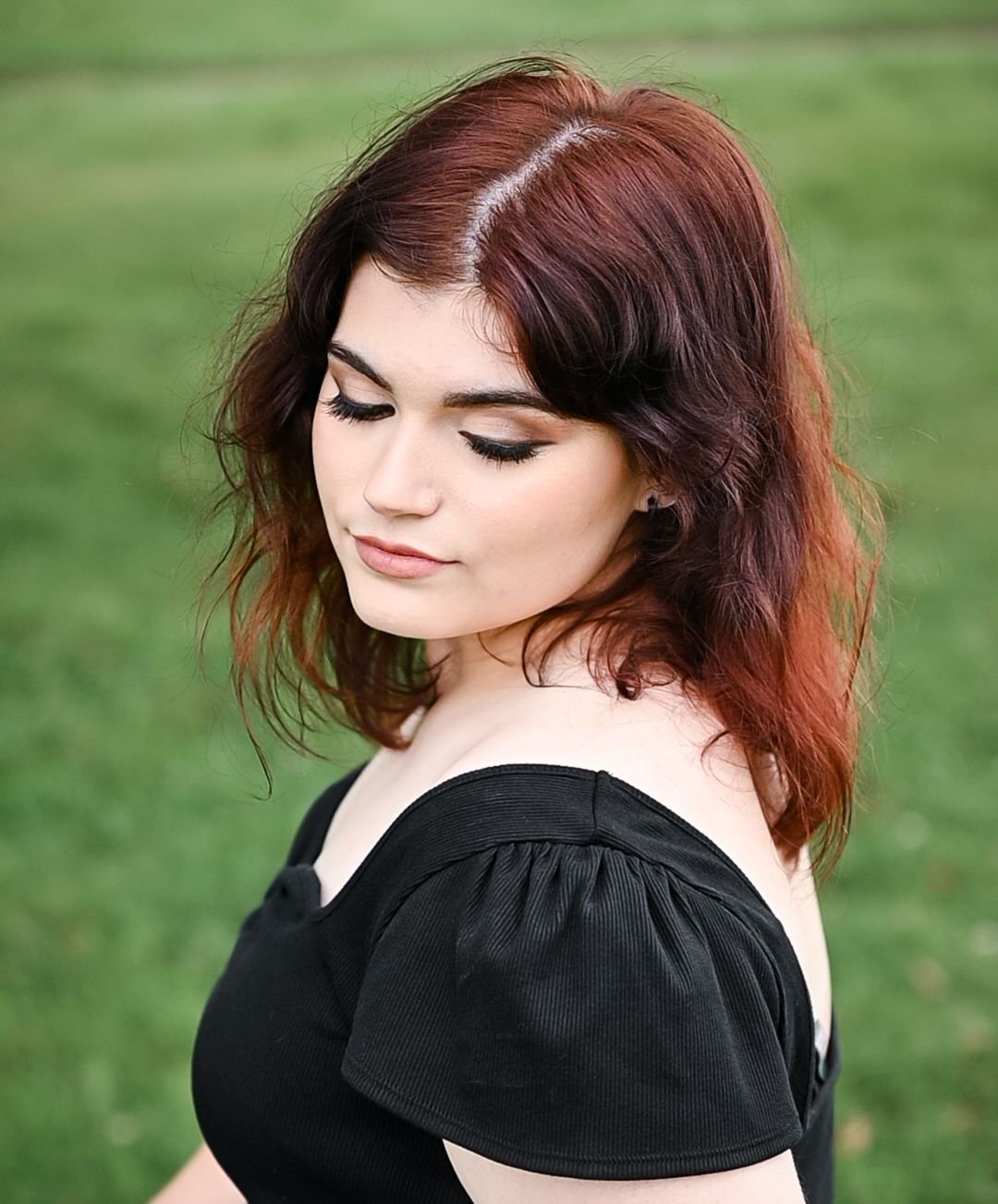 Side profile portrait against green background featuring black off-shoulder dress and flowing hair.