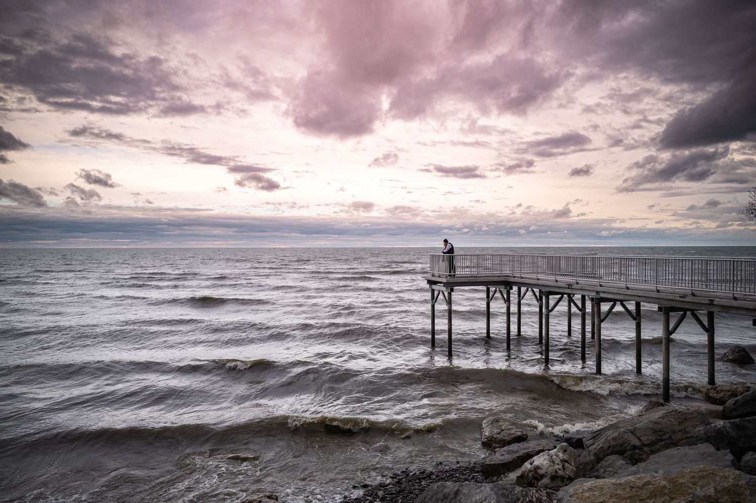 Moody landscape photo of pier extending into choppy waters under dramatic purple sky.