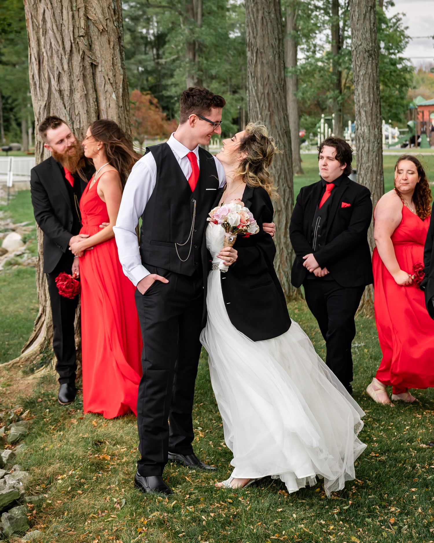 Wedding party poses together near pine trees with bridesmaids in red dresses.