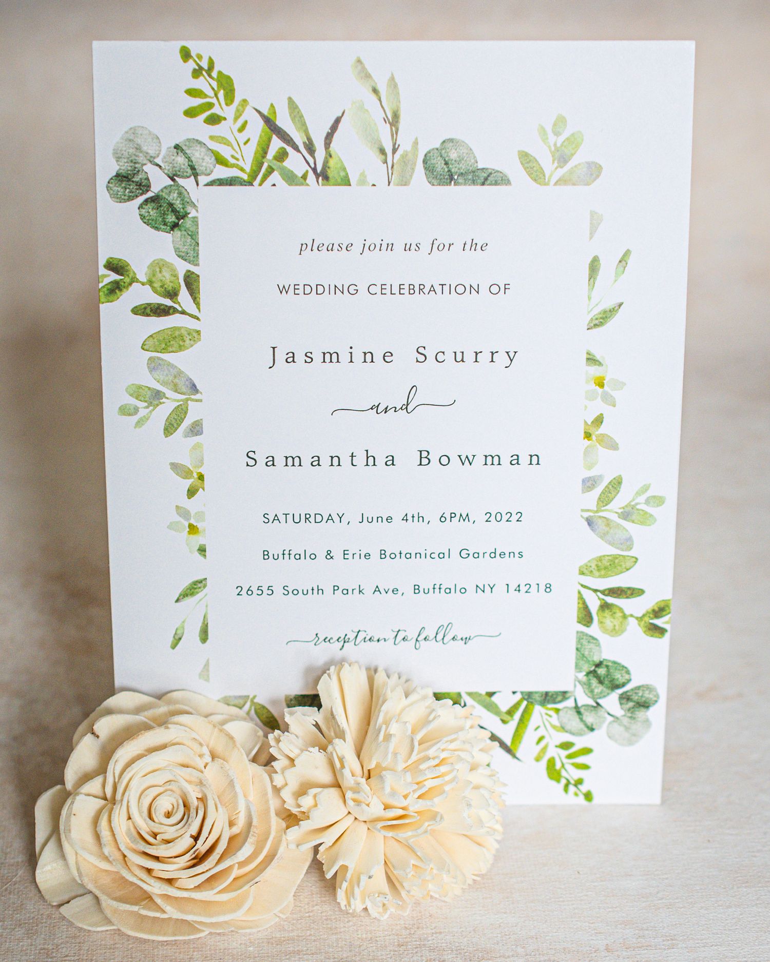 Elegant wedding invitation with watercolor greenery design and cream-colored paper flowers.