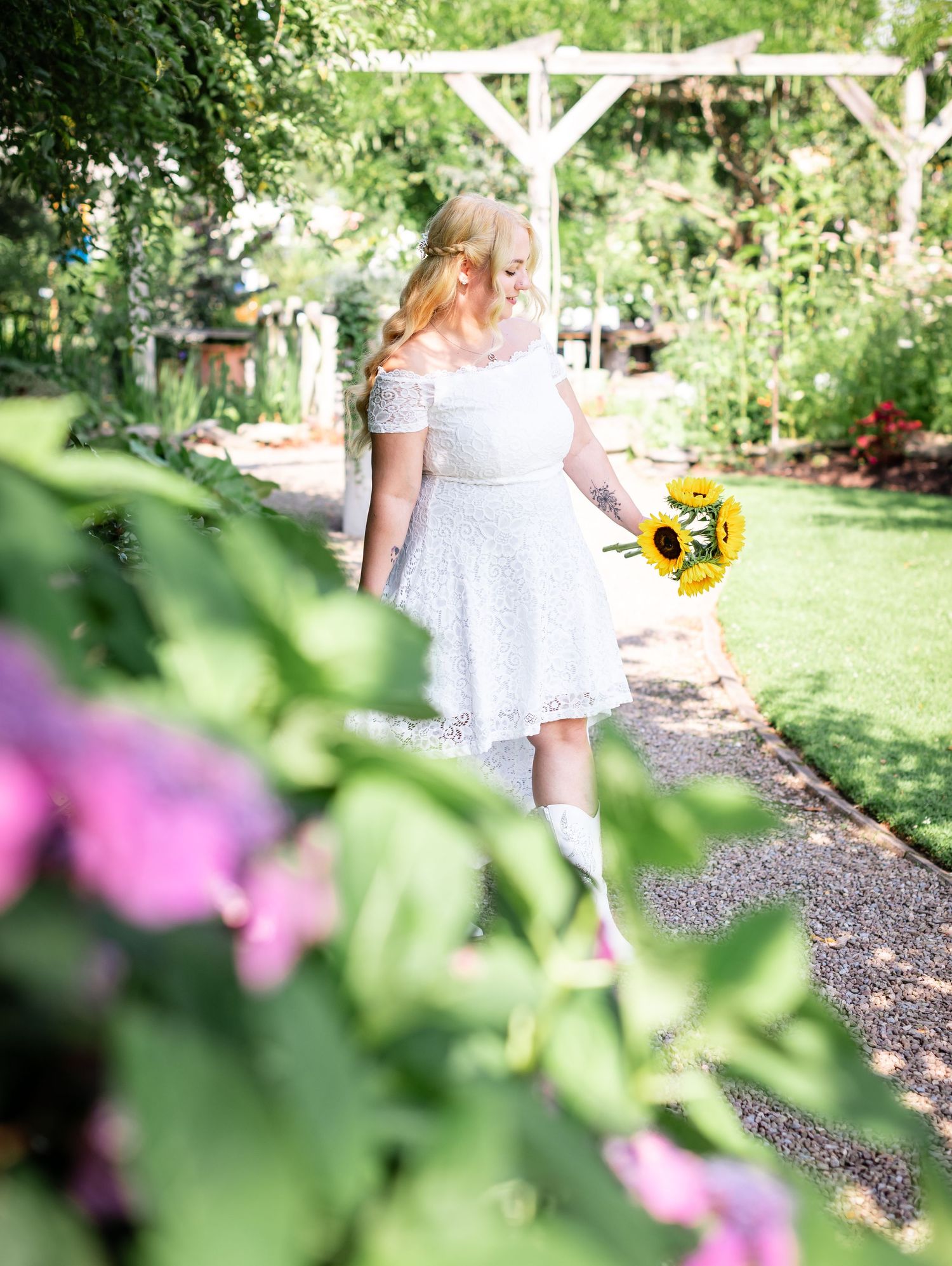 A white lace dress in a garden setting with yellow sunflowers and pink flowers in the background.