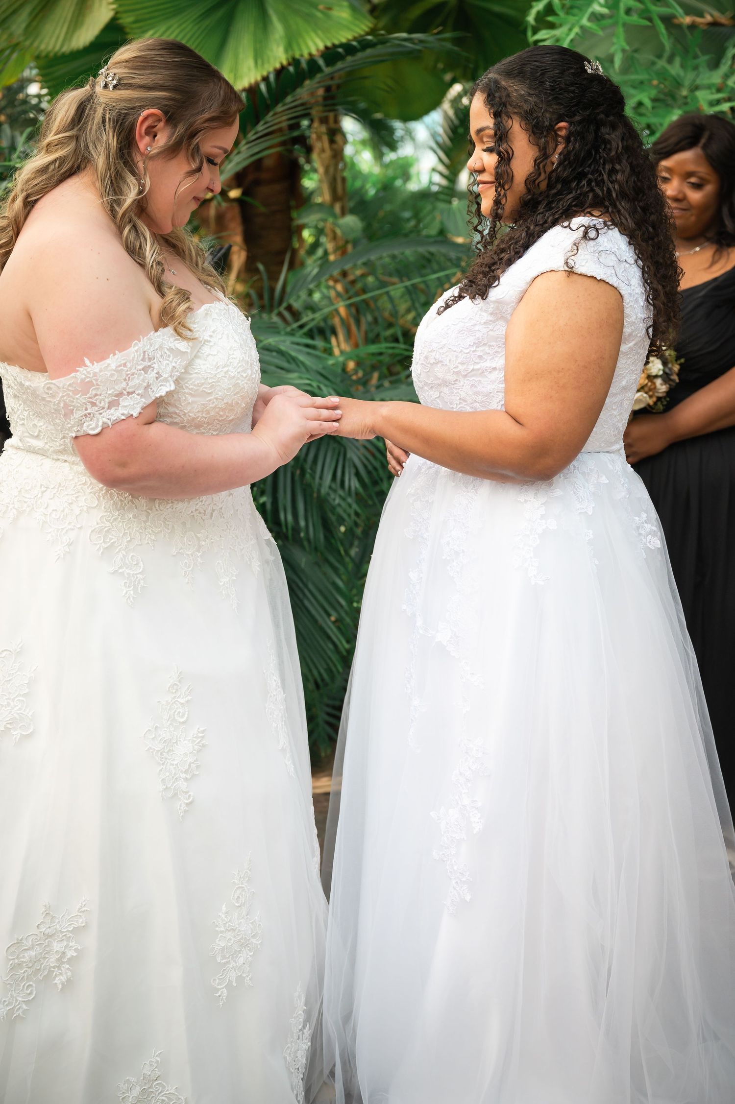 Two people in white wedding gowns exchange rings during a ceremony.