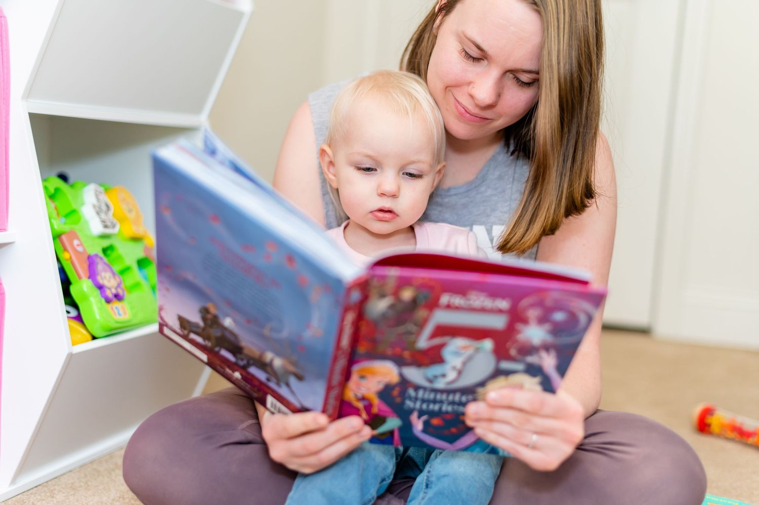 Adult and child sit together reading a colorful storybook in a playroom setting.