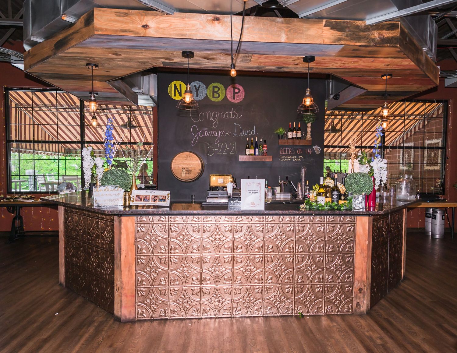 A rustic bar setup with copper accents, wooden floors, and industrial ceiling details.
