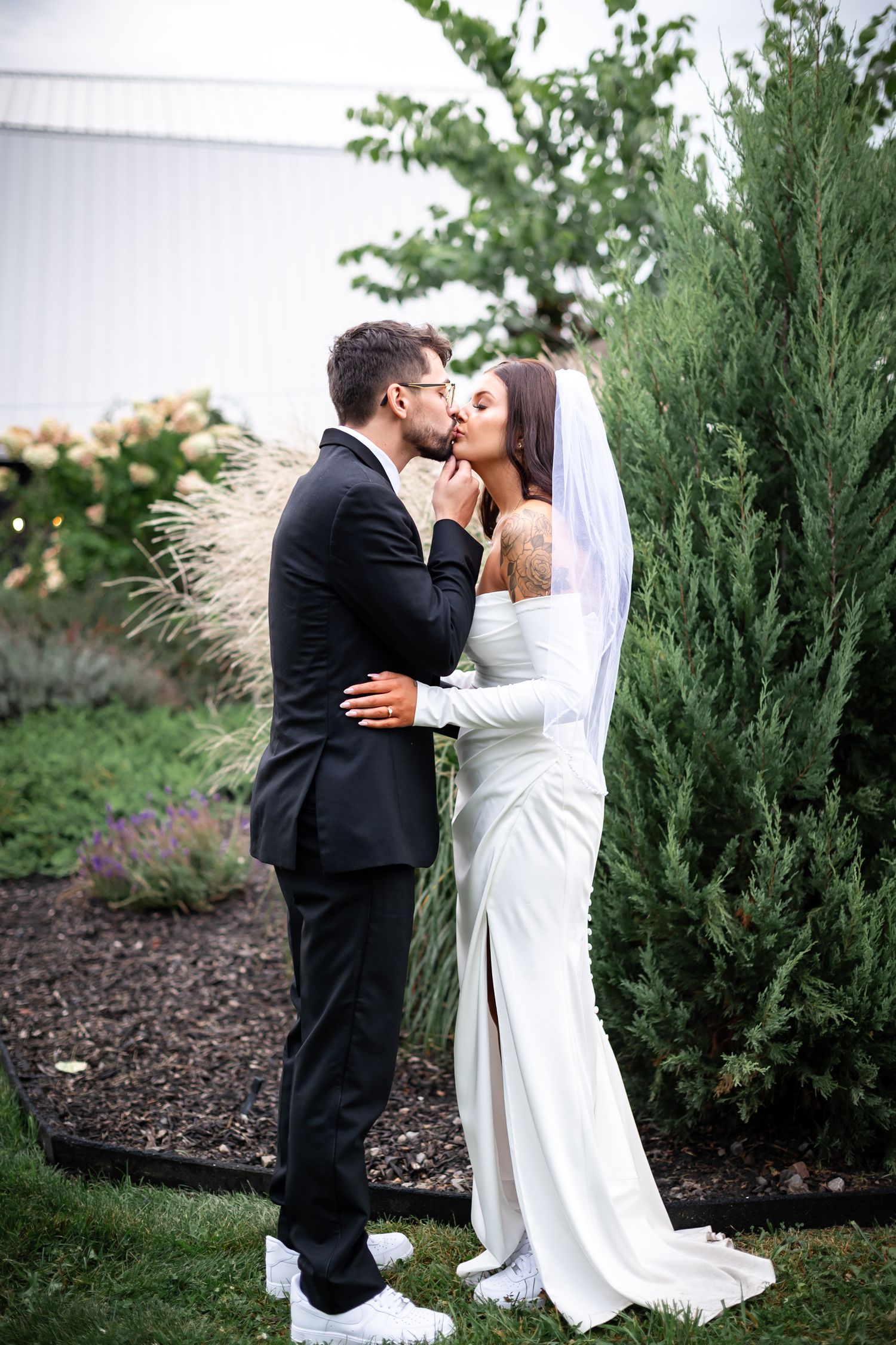A tender wedding moment captured in a garden setting with evergreen trees.