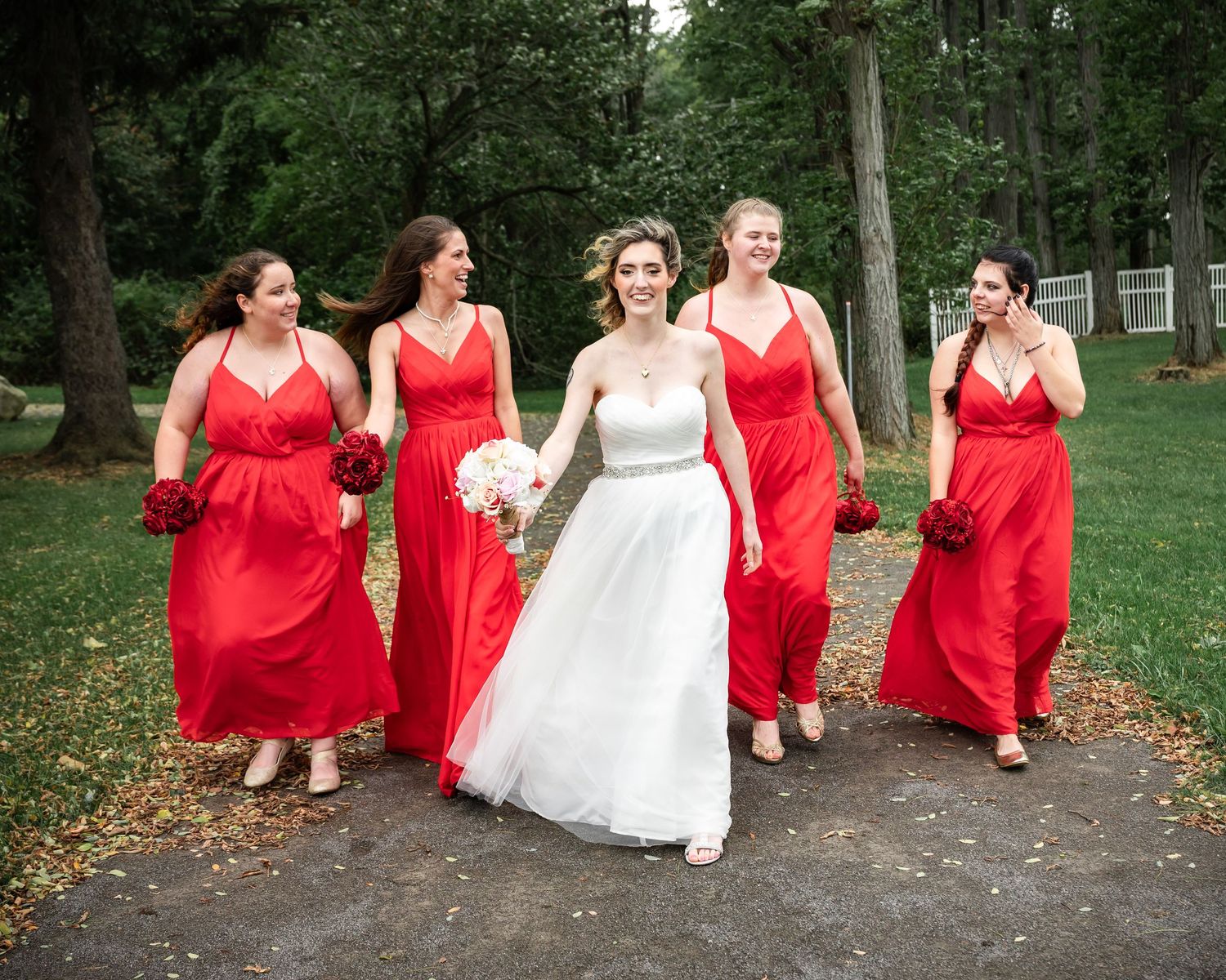 Wedding party walking together on path with bridesmaids in flowing red gowns.