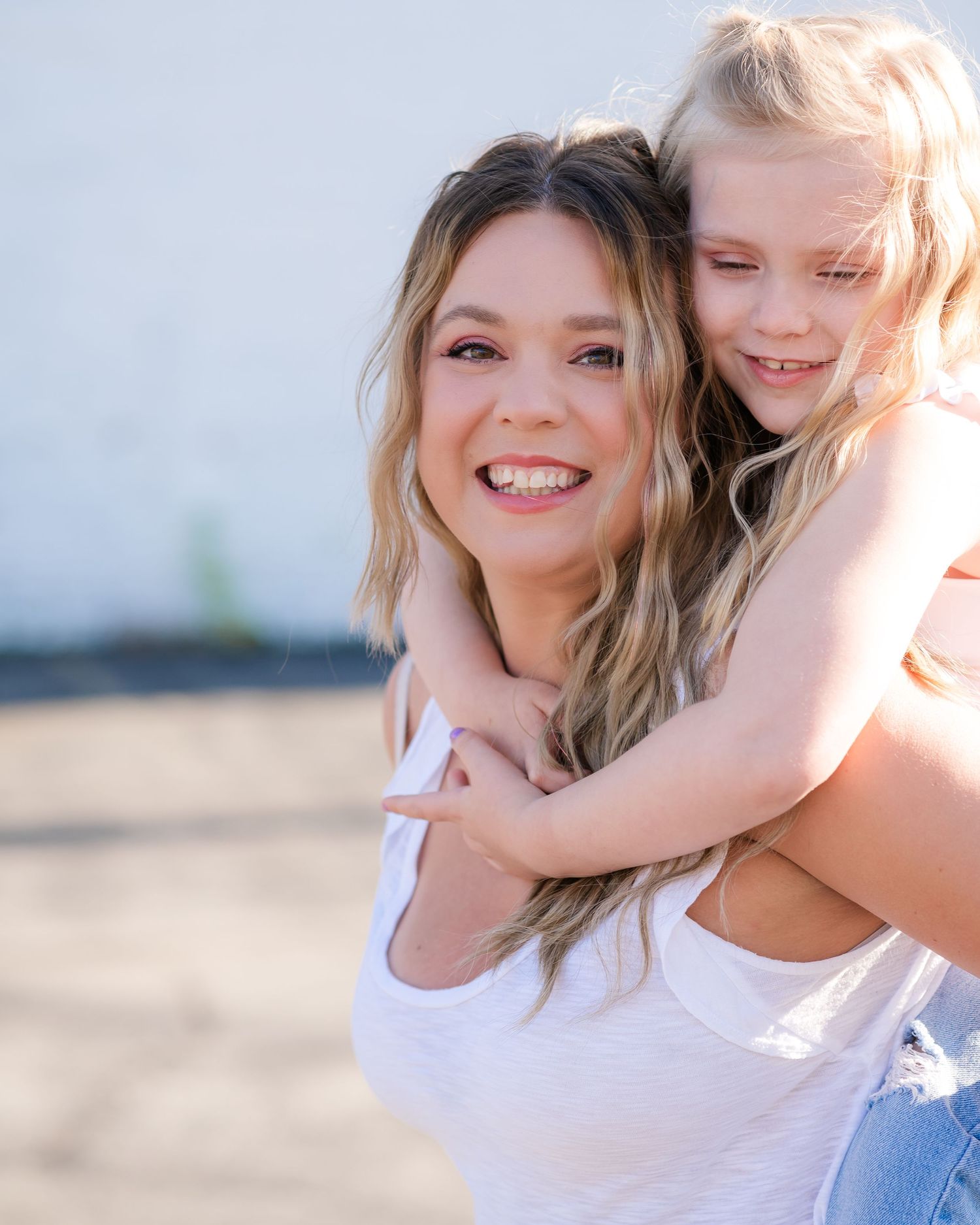 A joyful mother and daughter share a playful piggyback ride moment outdoors in natural sunlight.