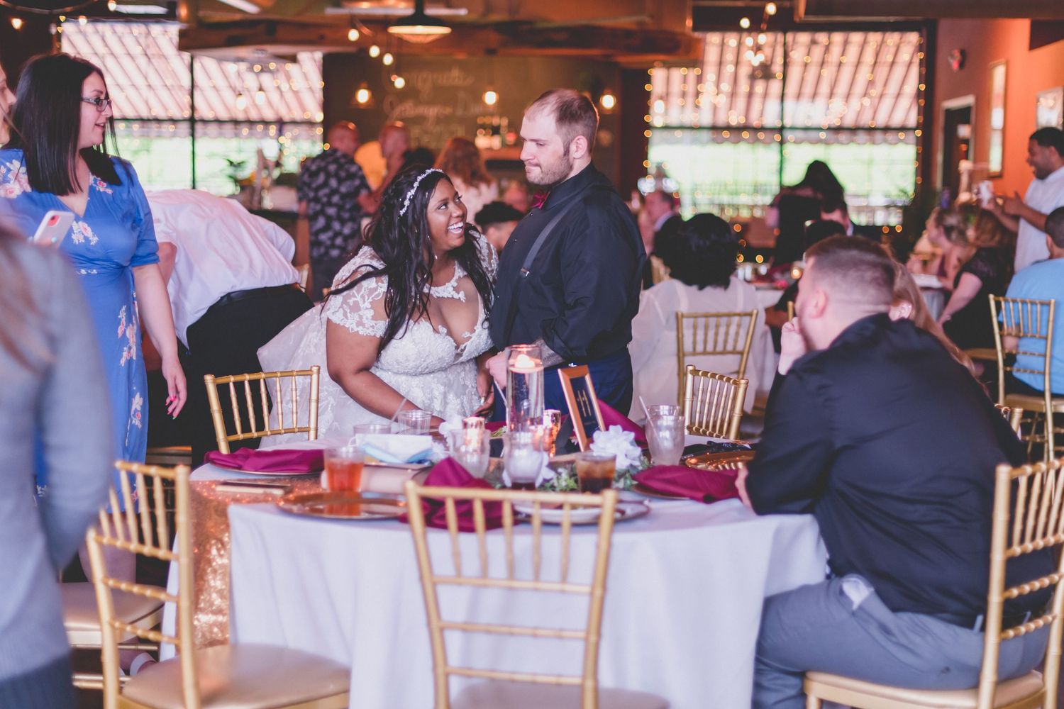 Guests enjoying a wedding reception at tables decorated with red accents in an indoor venue.