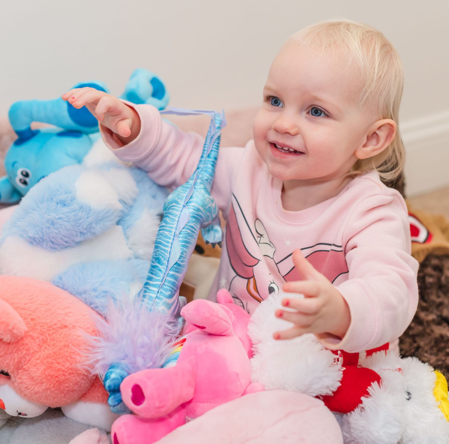 Baby playing with blue and pink plush toys while wearing pink clothing.