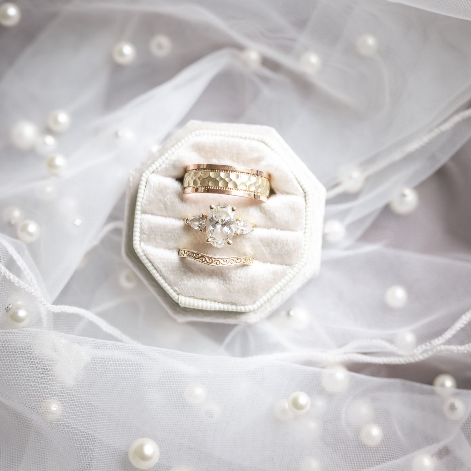 Gold wedding rings displayed in an ivory velvet octagonal ring box on a white veil with pearl accents.