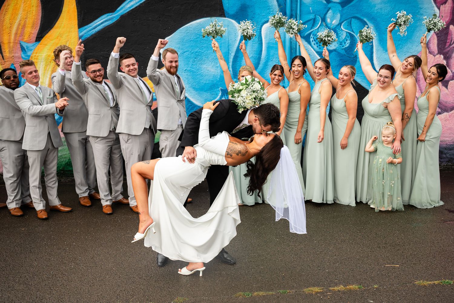 Wedding party poses with bright blue graffiti wall backdrop in an energetic and fun group shot.