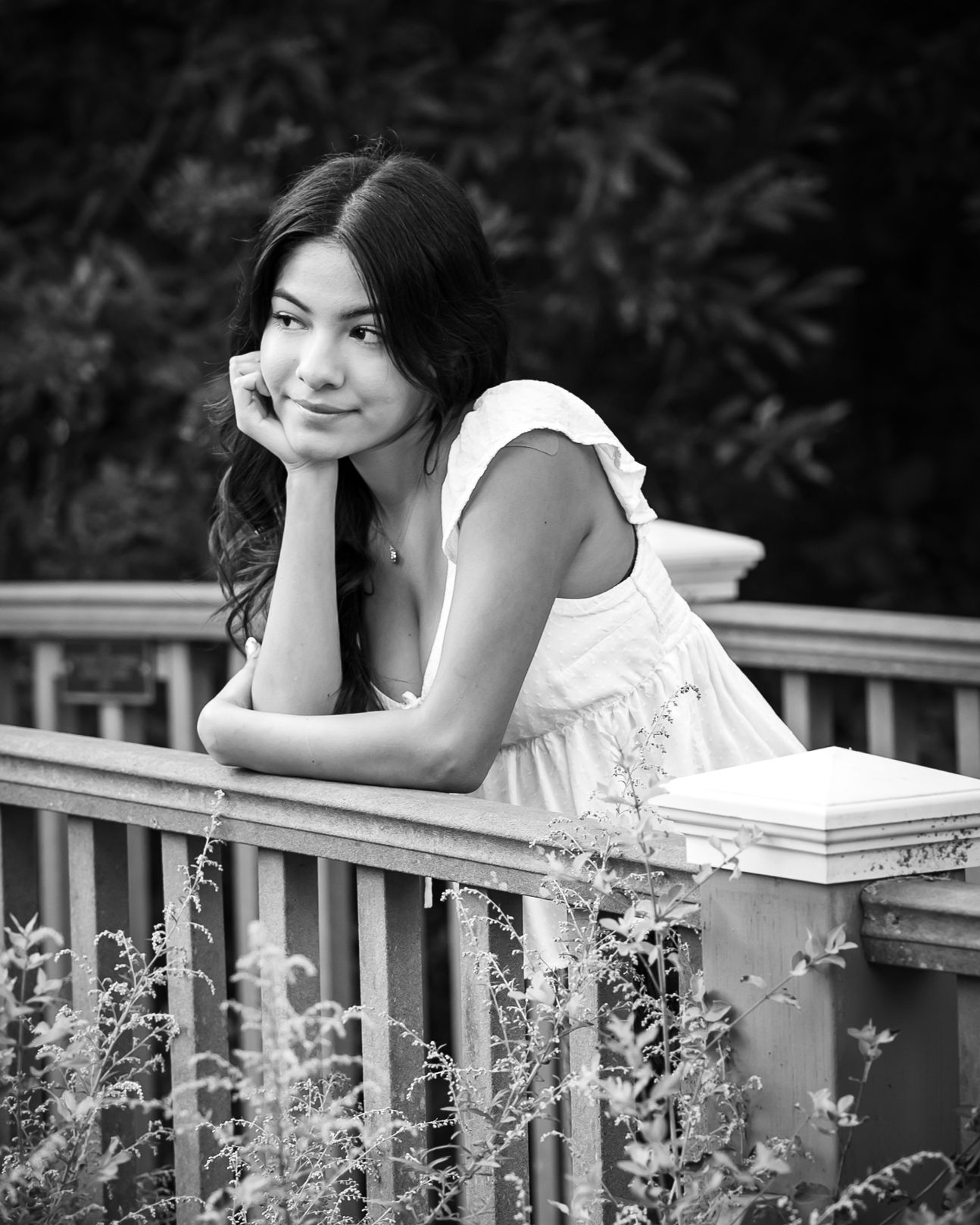 Black and white portrait of woman leaning on railing in natural setting.