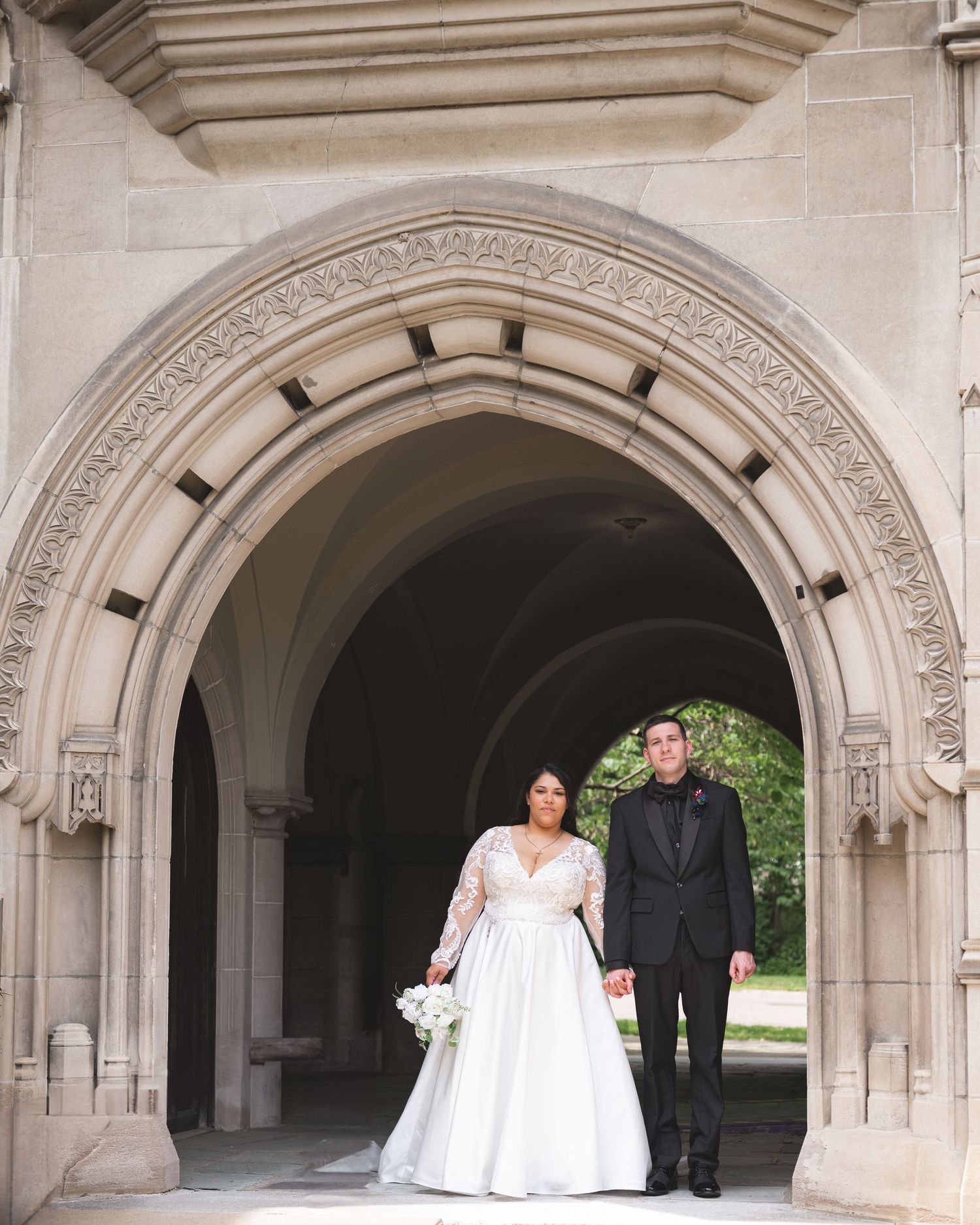 A couple poses under a series of stone archways on a sunny day during their wedding ceremony.