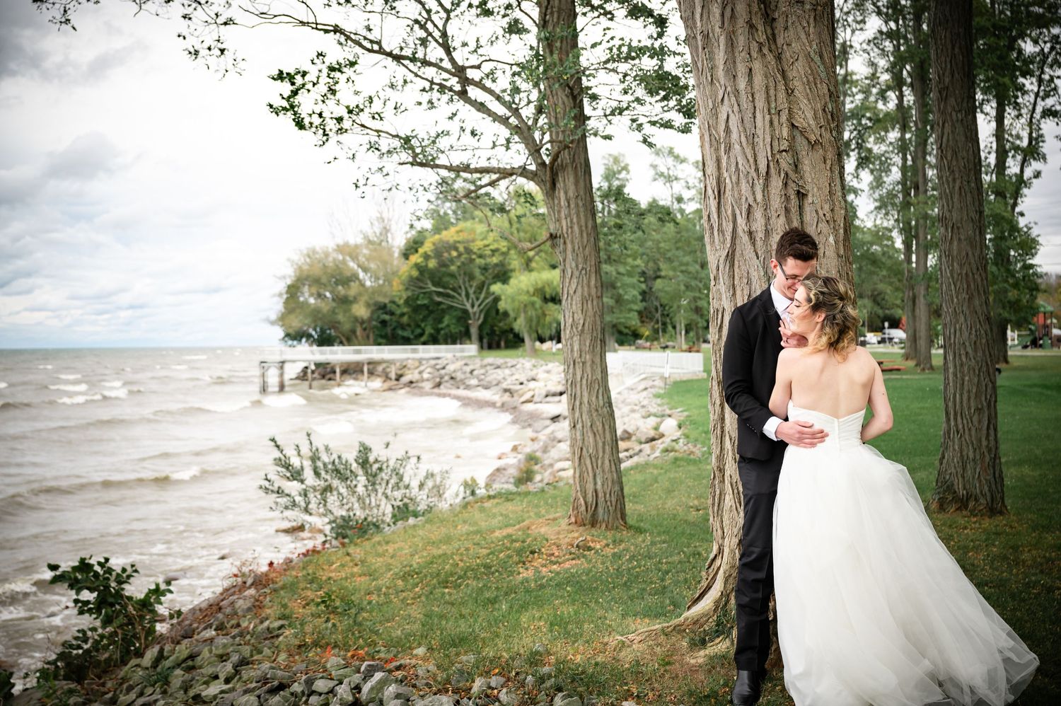 Elegant wedding photo on a beach shoreline with tall trees framing the scene.