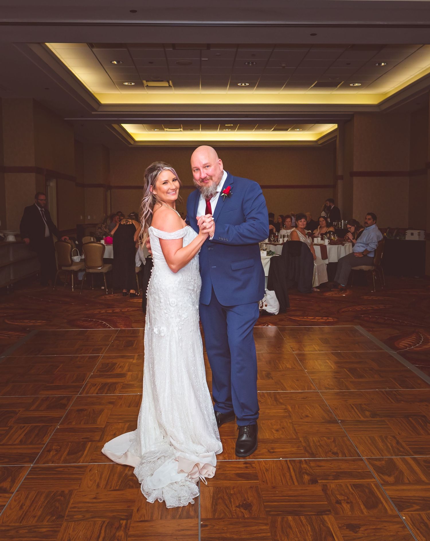 A couple shares a dance moment on a wooden floor during their wedding reception.