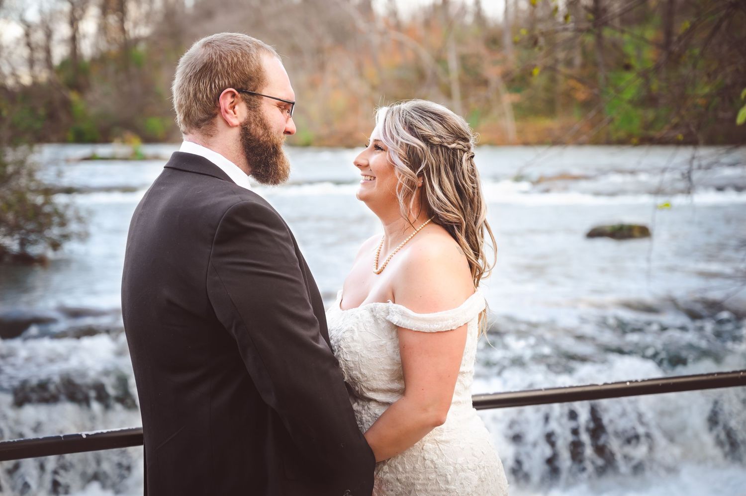 Romantic moment between newlyweds against backdrop of flowing waterfall and autumn scenery.