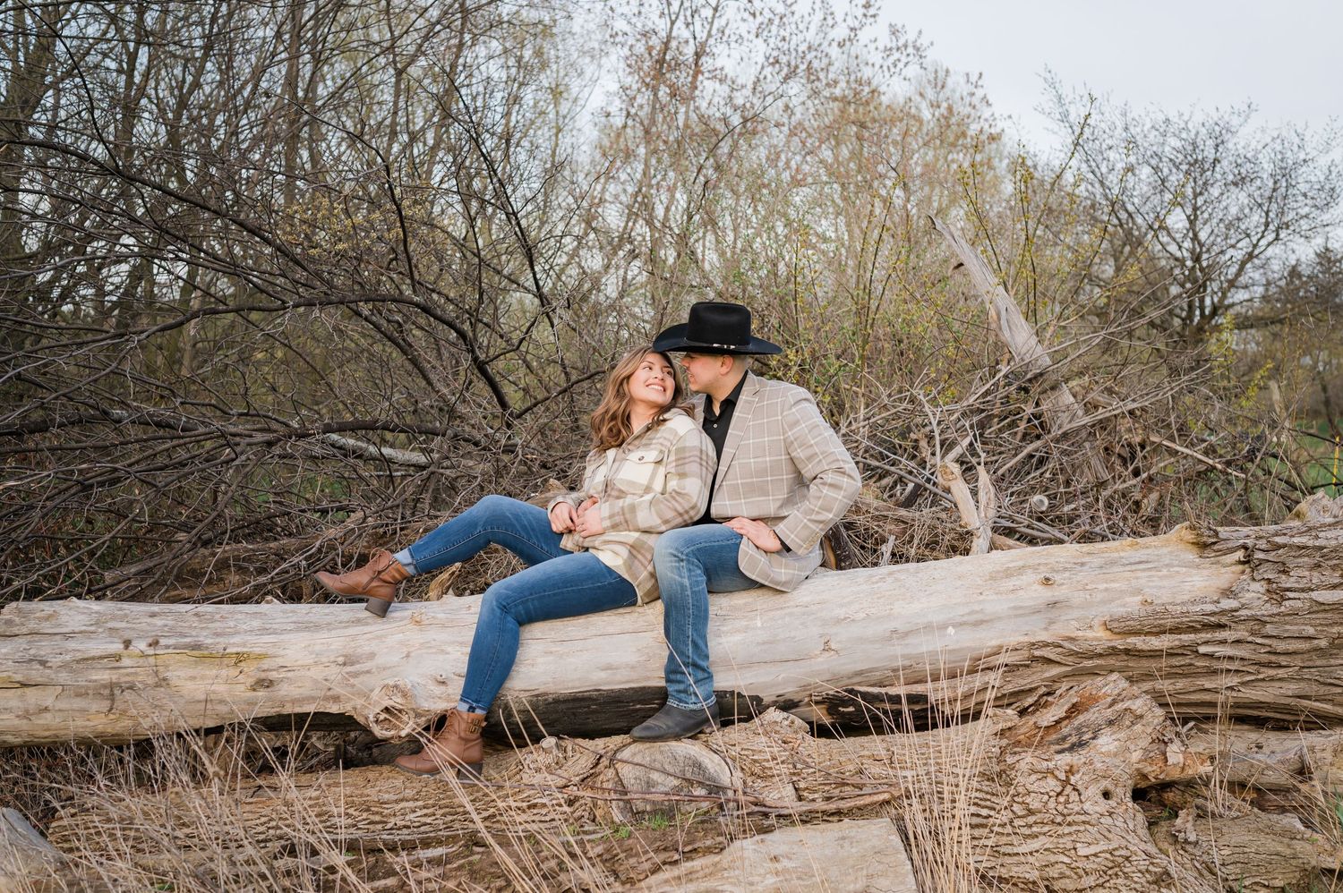 A couple shares an intimate moment while sitting on a fallen log in nature.