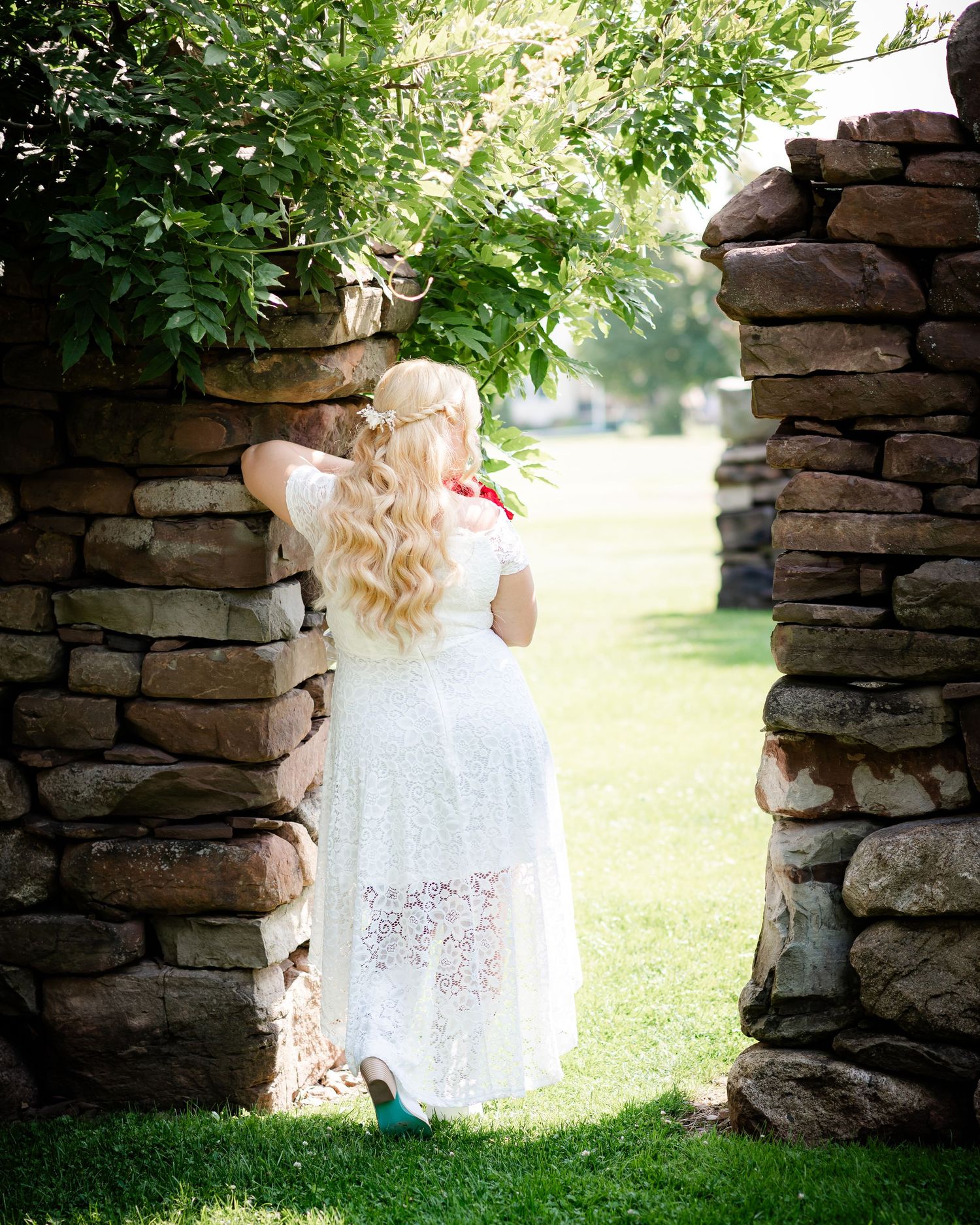 White lace dress framed by rustic stone archway in a garden setting.