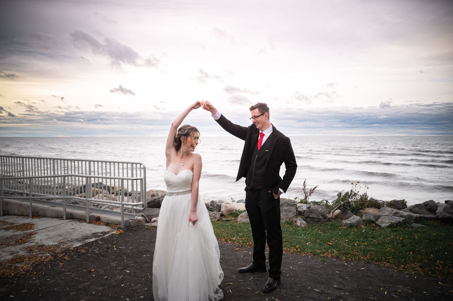 A couple dancing together by the ocean at sunset with cloudy skies in the background.