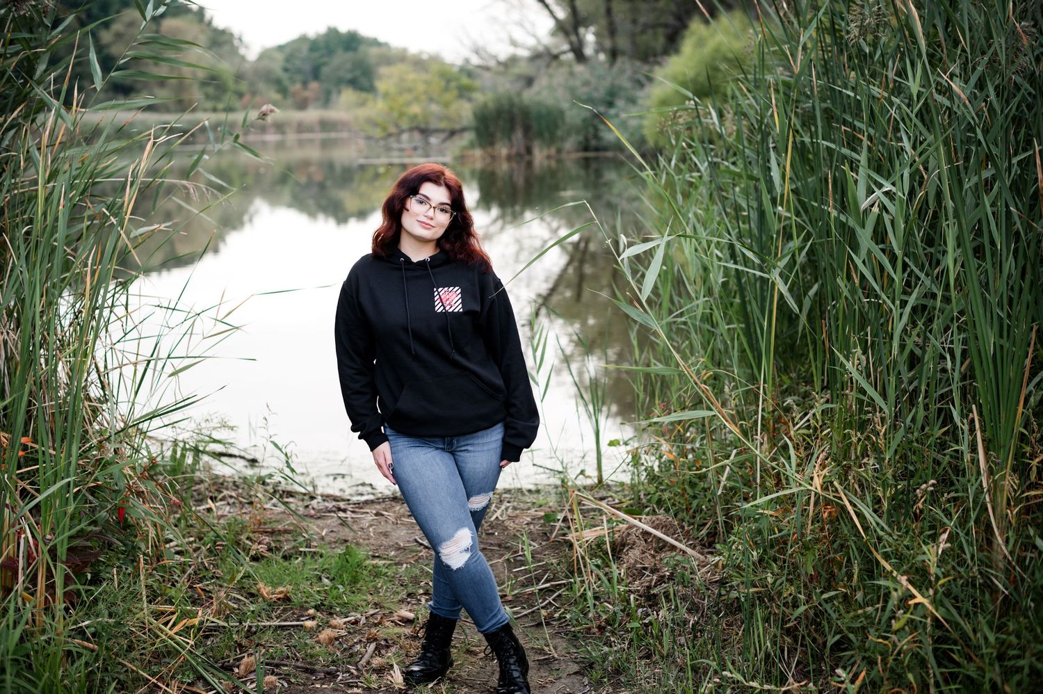 Casual portrait by a pond with cattails and water reflection in natural setting.