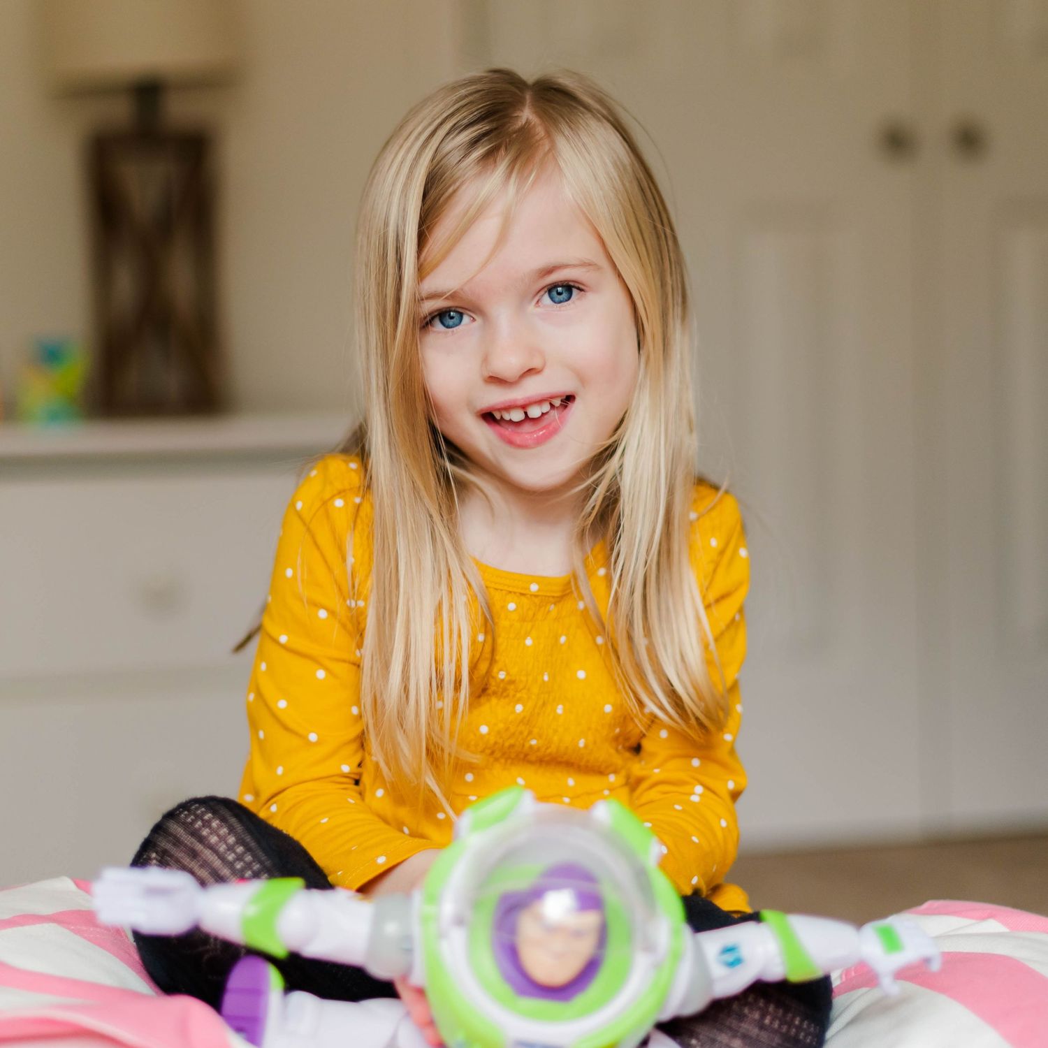 Young child in yellow dress smiles while playing with toys on a kitchen counter.