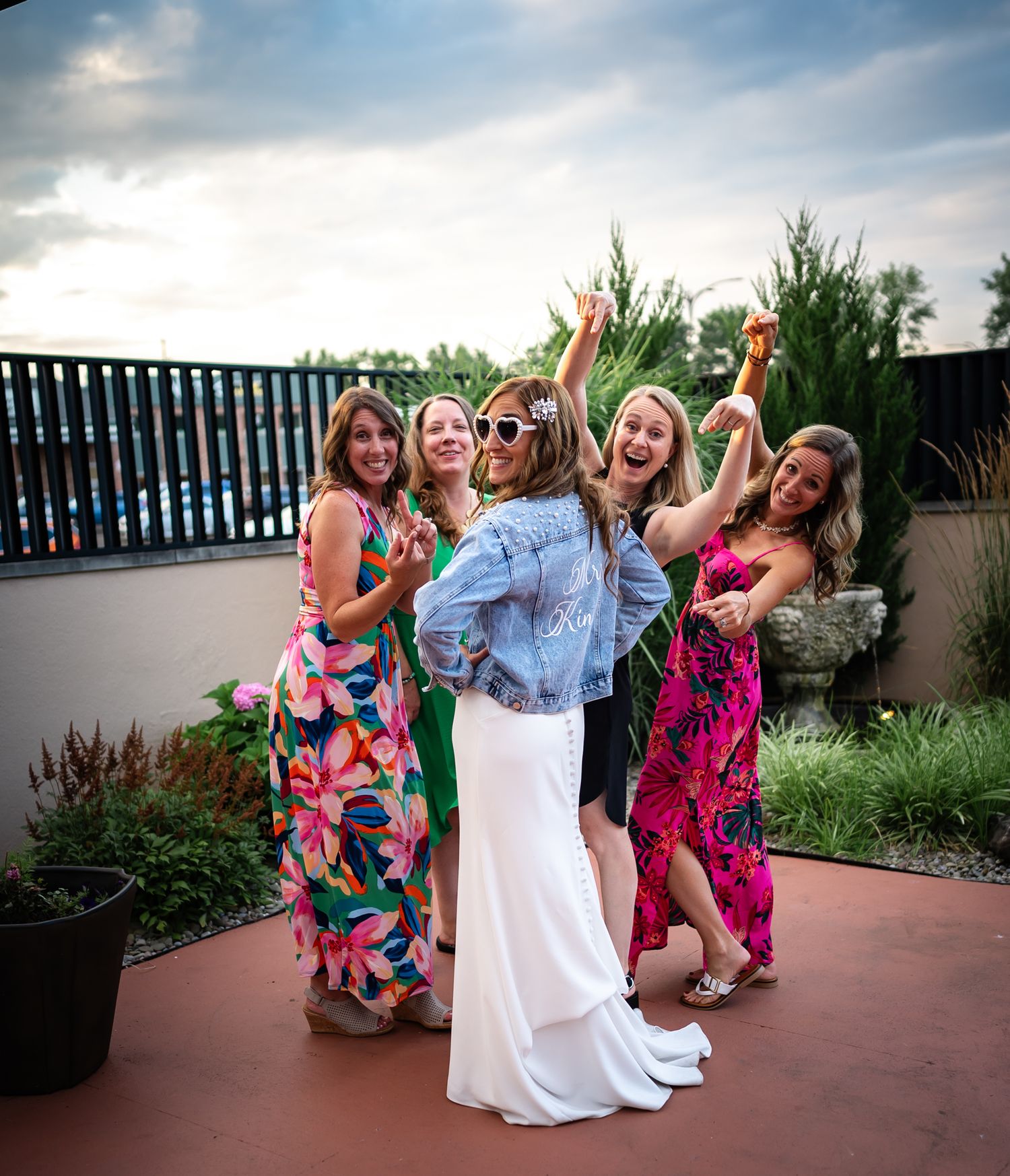 A group in colorful floral dresses celebrate together on an outdoor patio during a festive gathering.