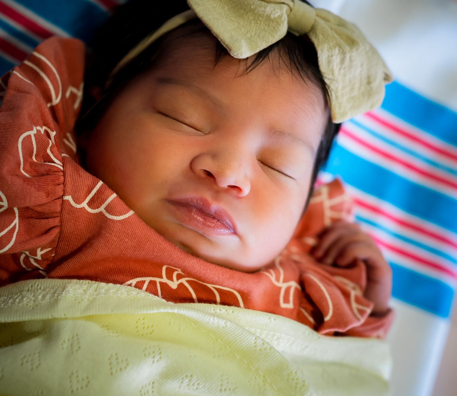 Sleeping newborn baby swaddled in brown and yellow blankets on a striped surface.