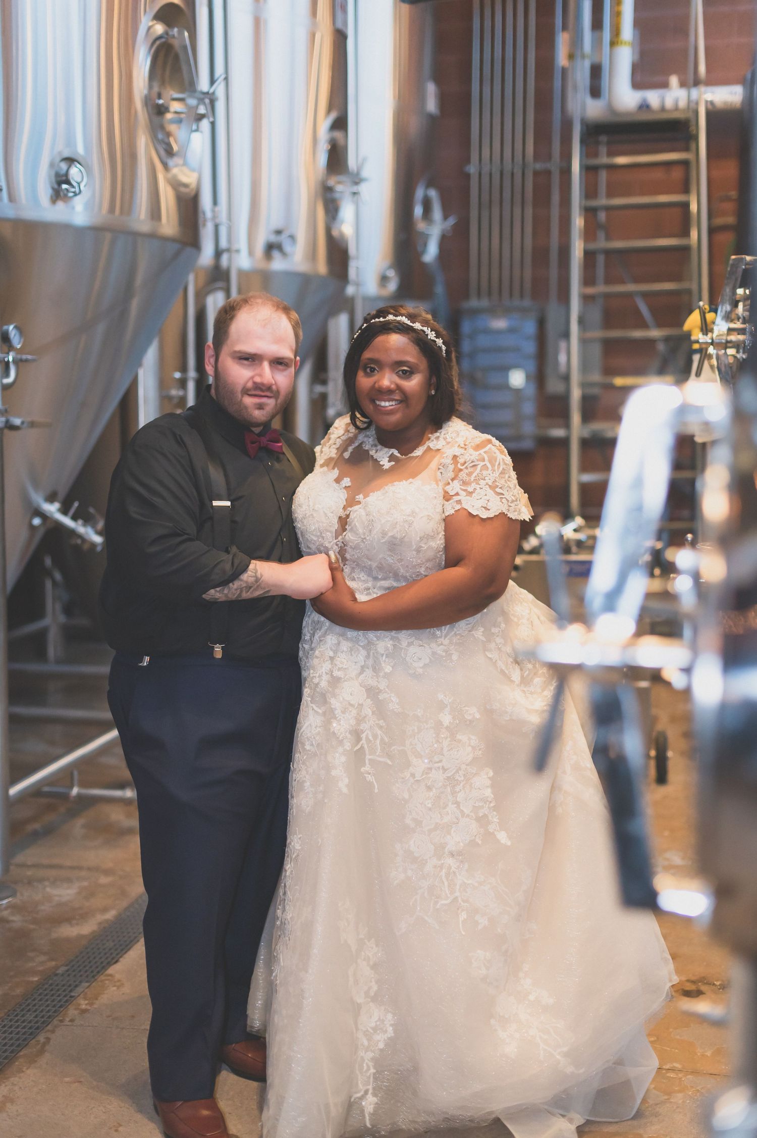 Wedding couple posing together in industrial brewery setting with steel tanks.